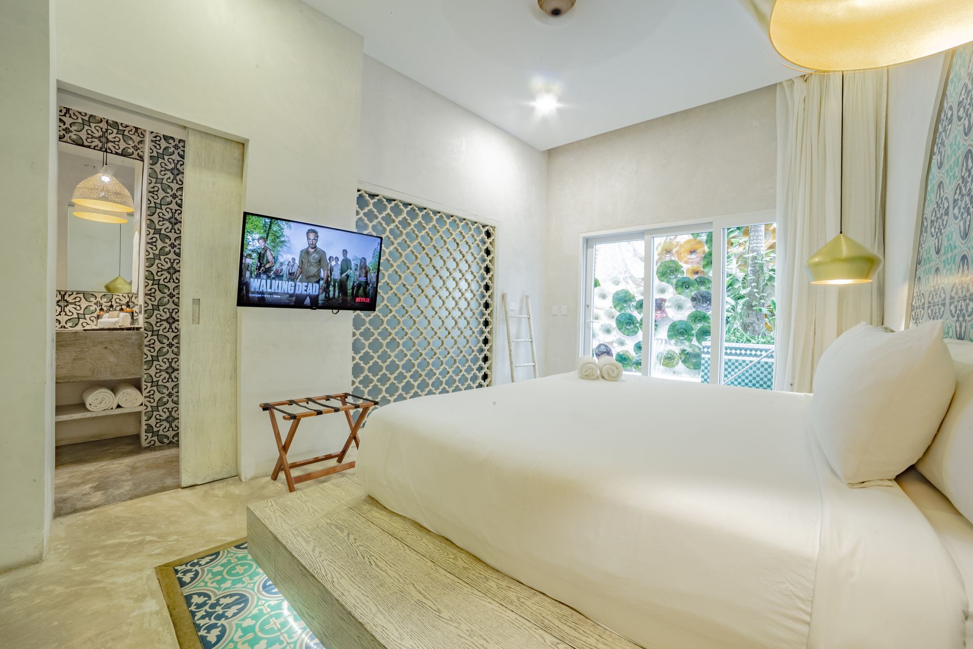 Bright bedroom with a king bed, TV, and bathroom. White and turquoise decor with outdoor view.