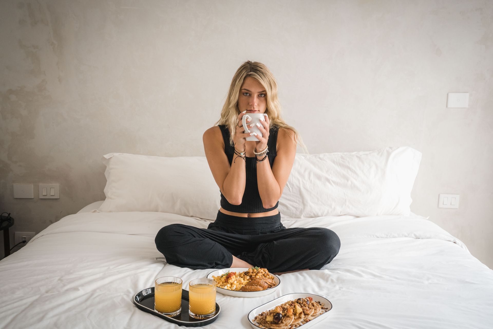 A woman is sitting on a bed drinking a cup of coffee.