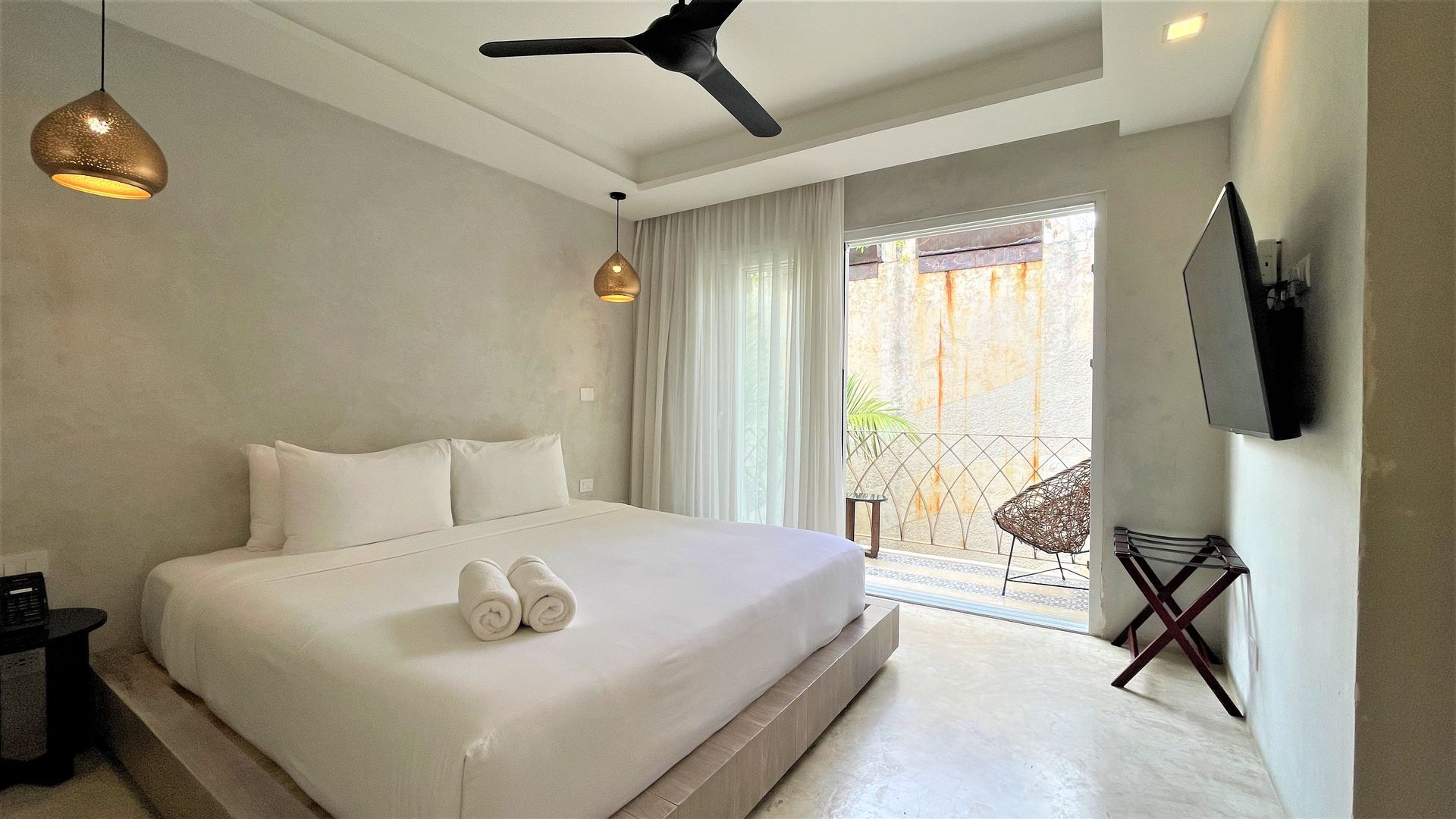 A hotel room with a large bed , ceiling fan , television and balcony.