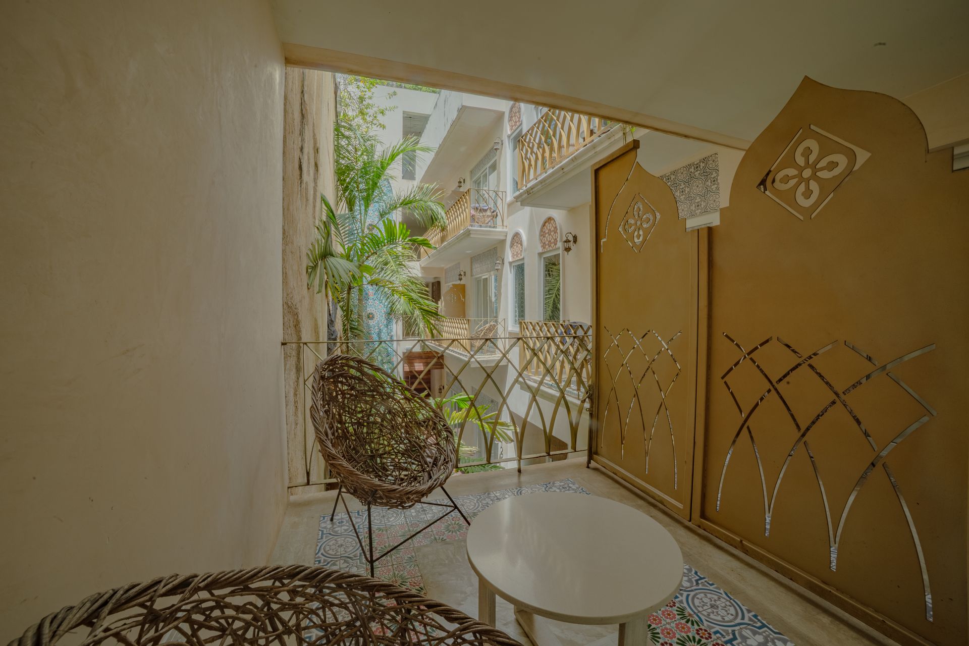 A small balcony with rattan chairs and a table overlooking a courtyard.