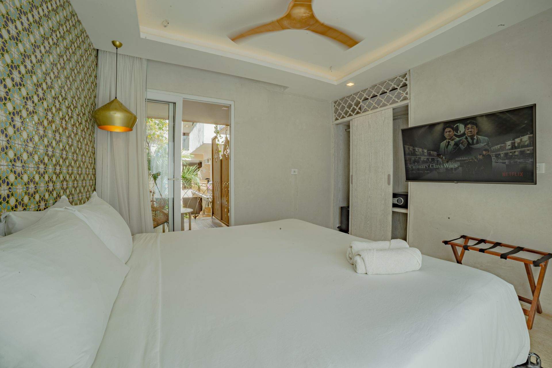 Dormitorio con cama grande blanca, TV, pared estampada y acceso al balcón.
