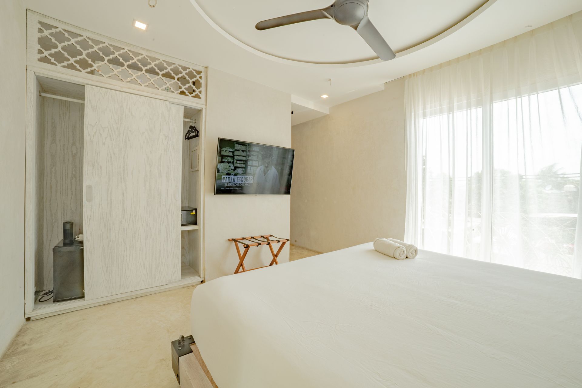 White bedroom with bed, closet, TV, window, and ceiling fan.