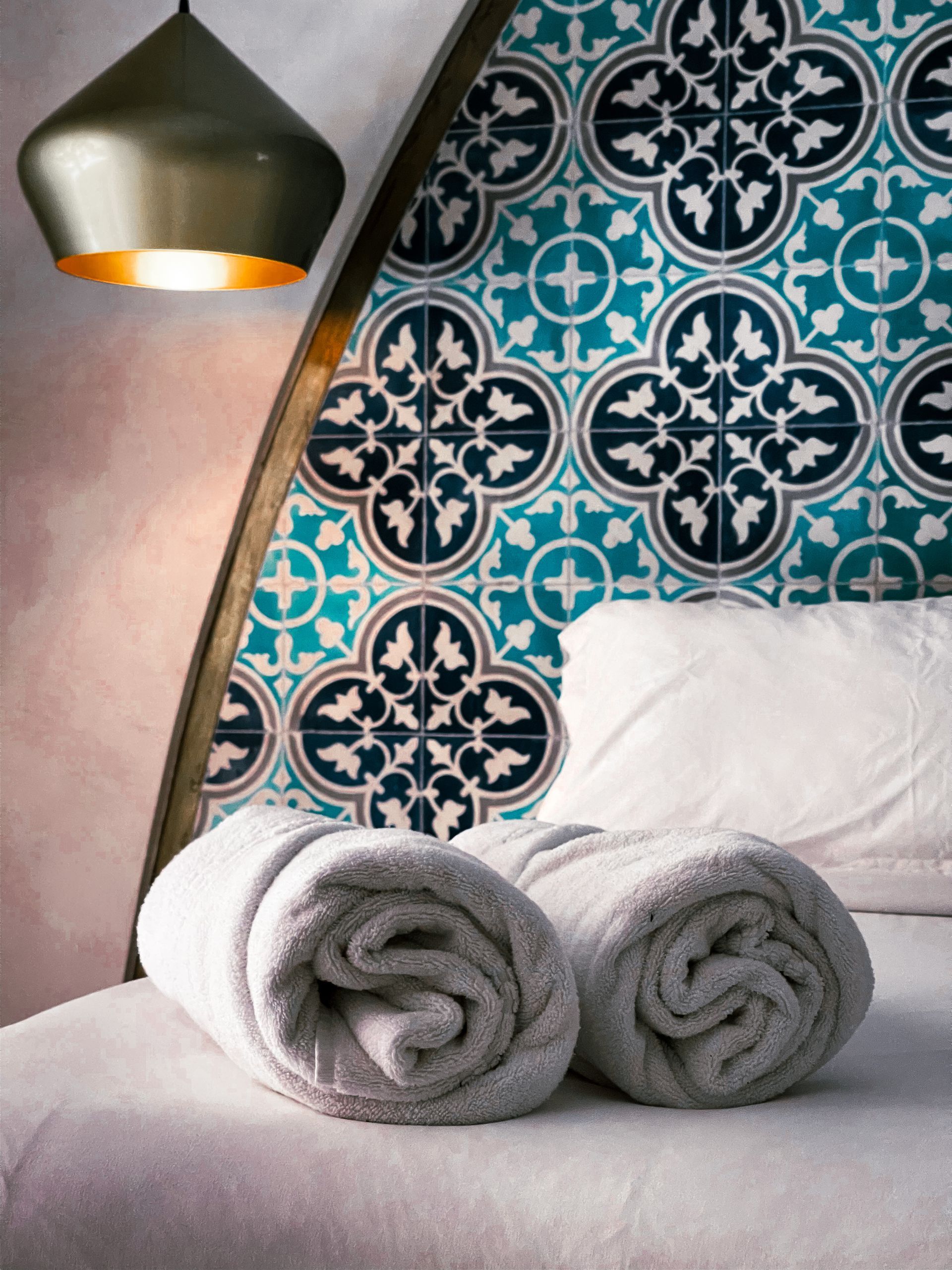 Two towels are rolled up on a bed in front of a tiled wall.