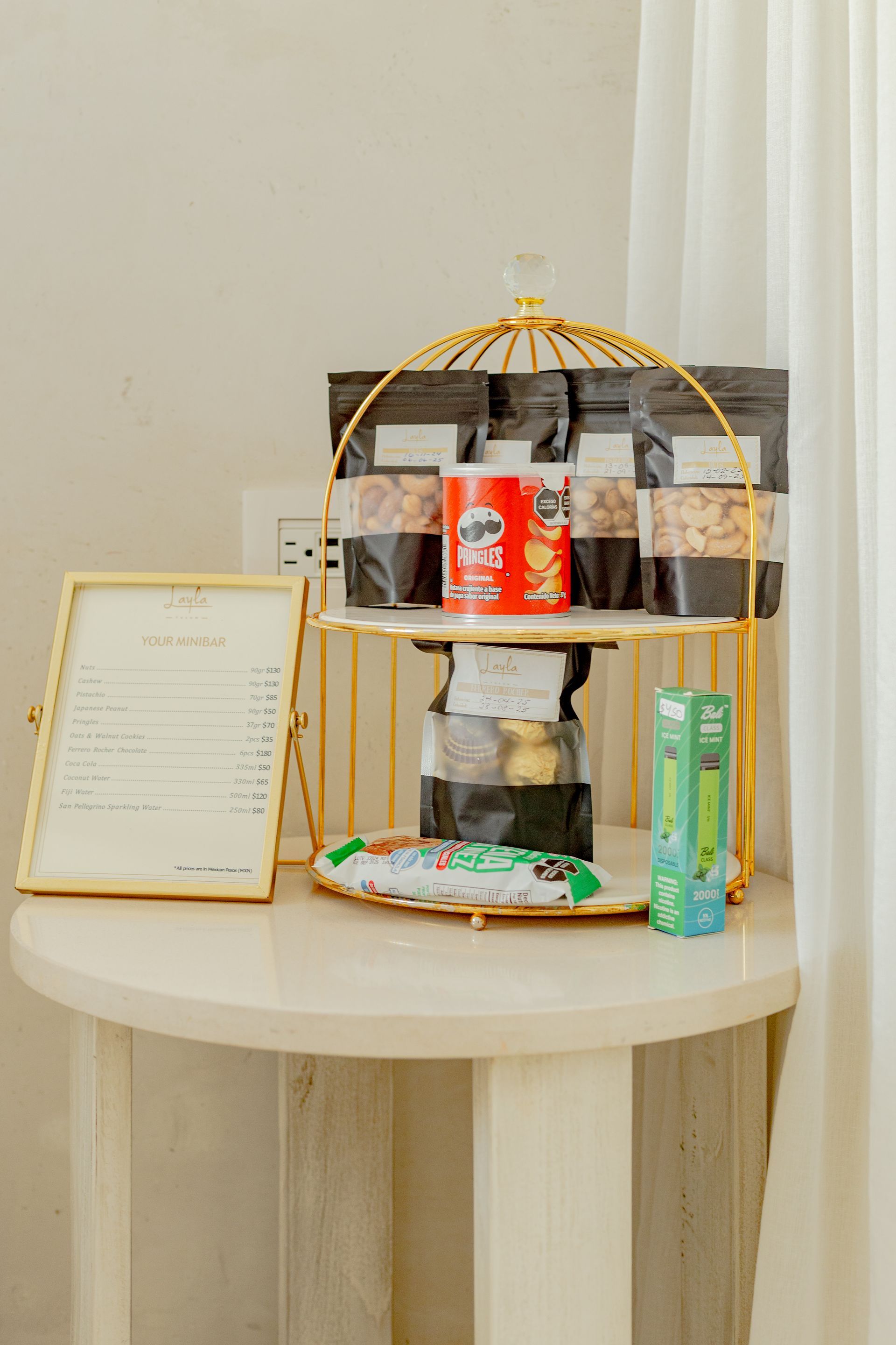 A small table holds snacks, a gold wire birdcage shelf, a framed menu, and a green tube.