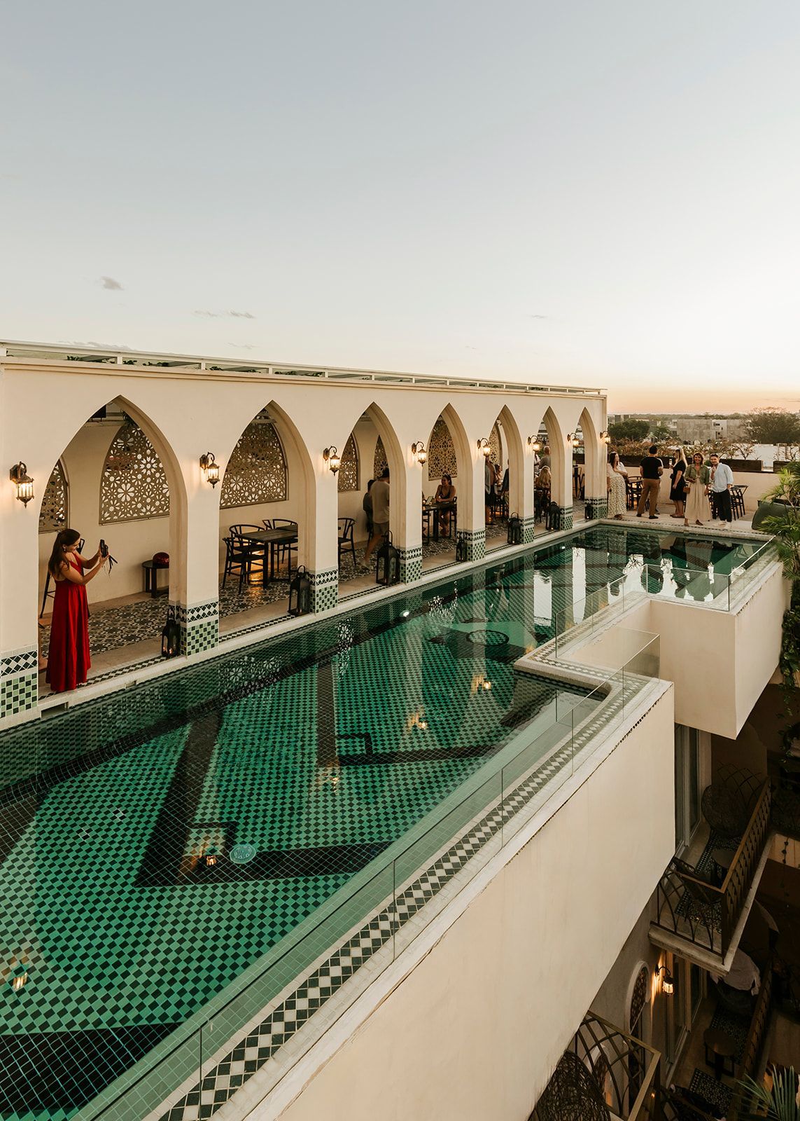 A woman in a red dress is standing next to a large swimming pool.
