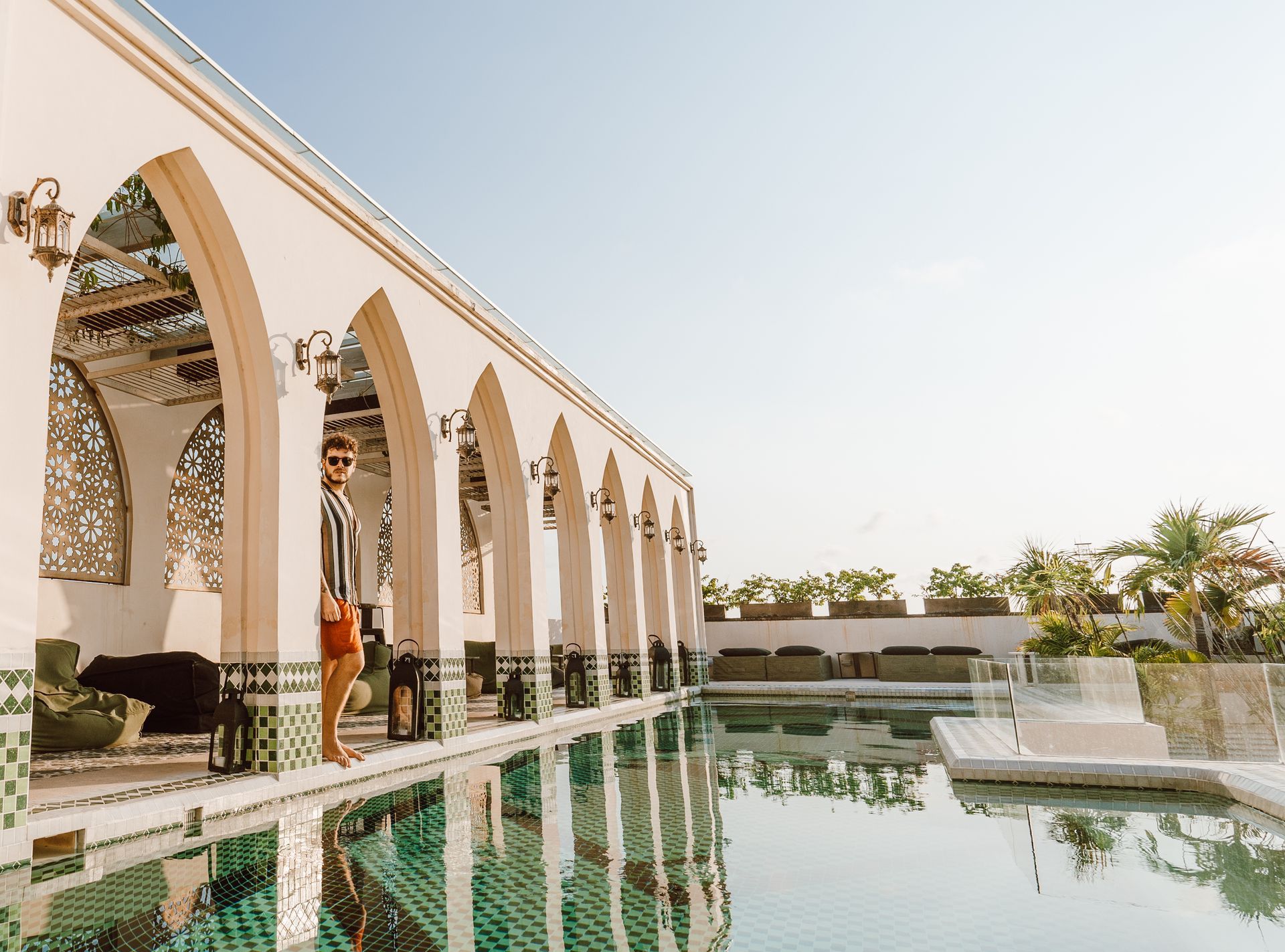 A woman is standing next to a swimming pool in front of a building.