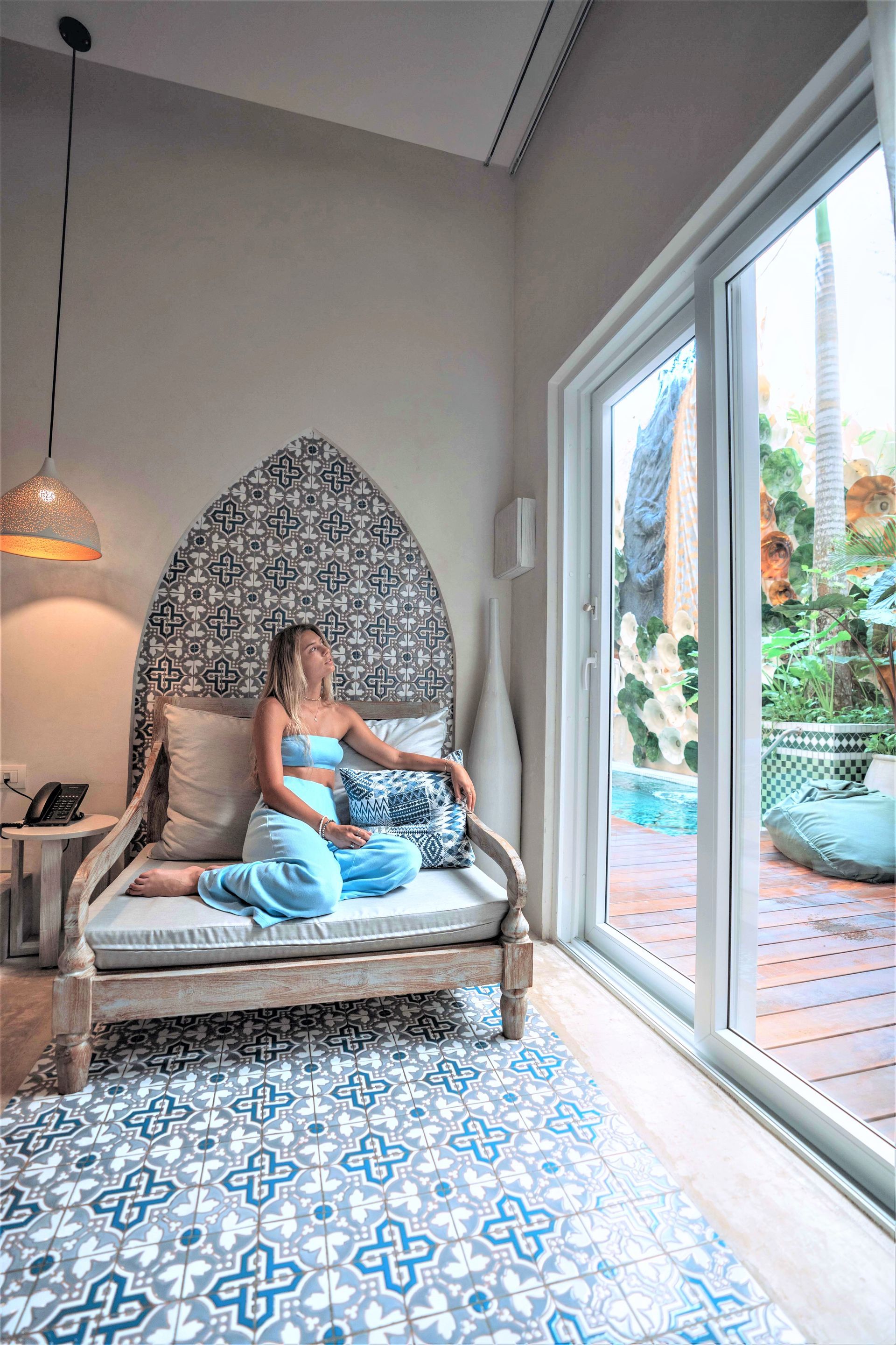 A woman is sitting on a couch in a room next to a window.