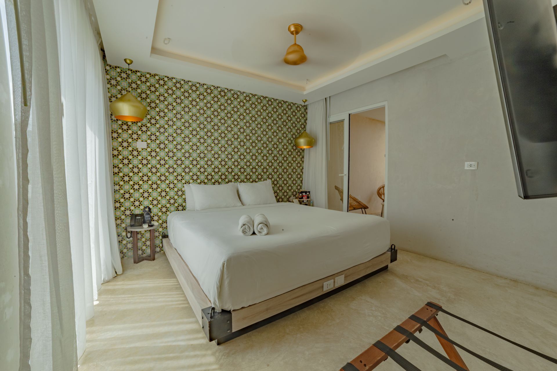 Bedroom with queen bed, patterned accent wall, gold light fixtures, and doorway to the ensuite.