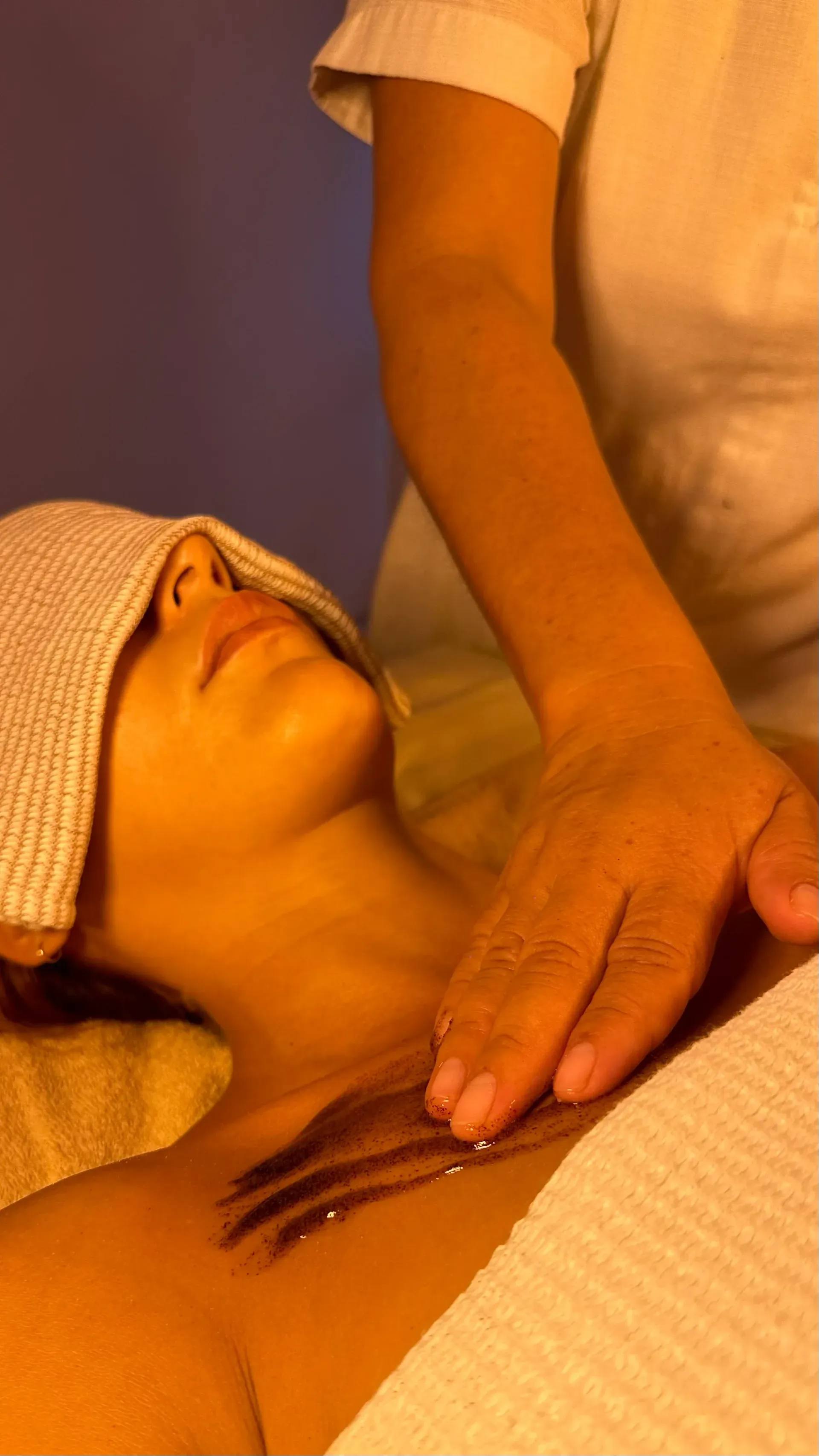 Woman receiving spa treatment, eyes covered, chest massage, warm lighting.