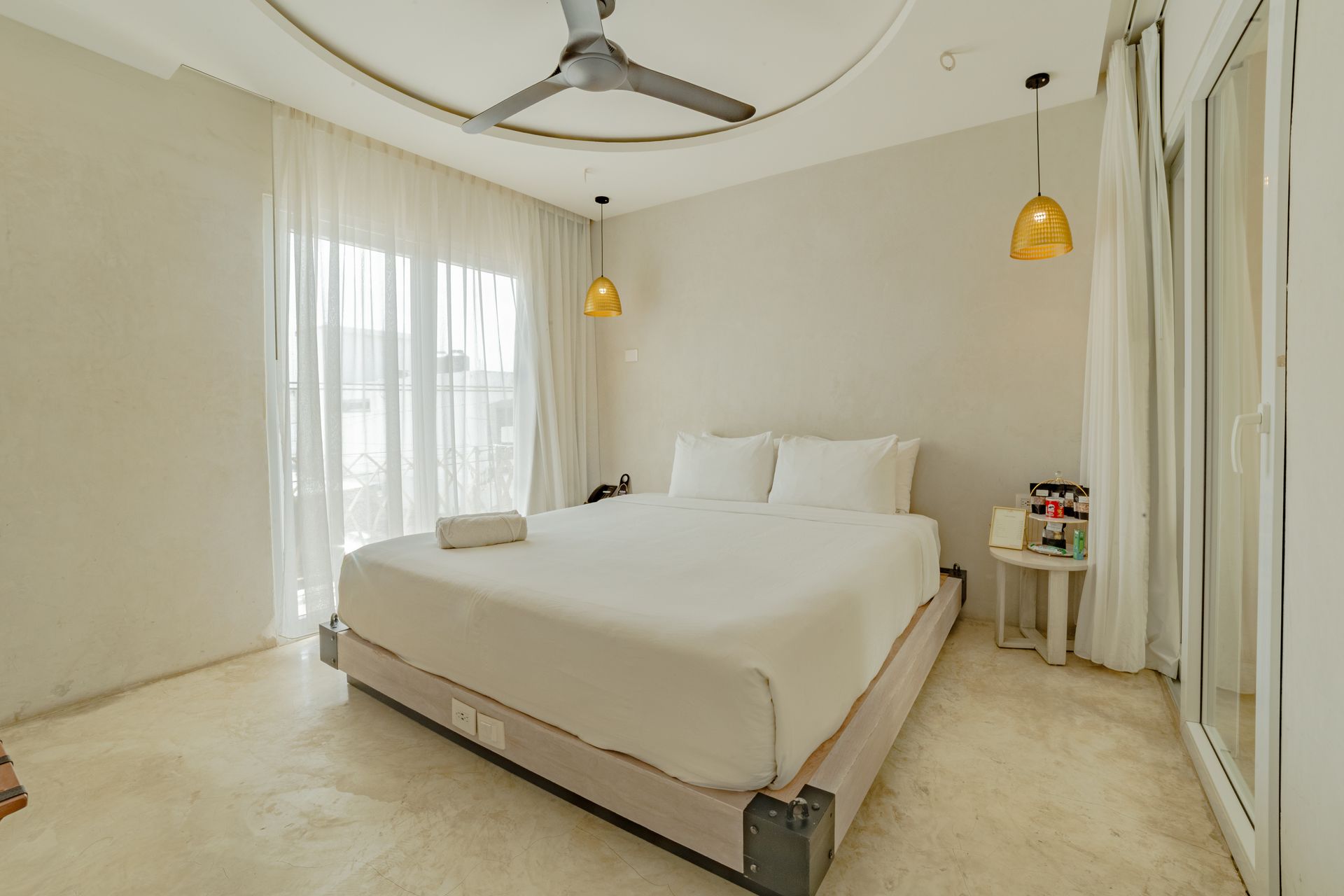 Bedroom with bed, sheer curtains, golden lamps, and ceiling fan.