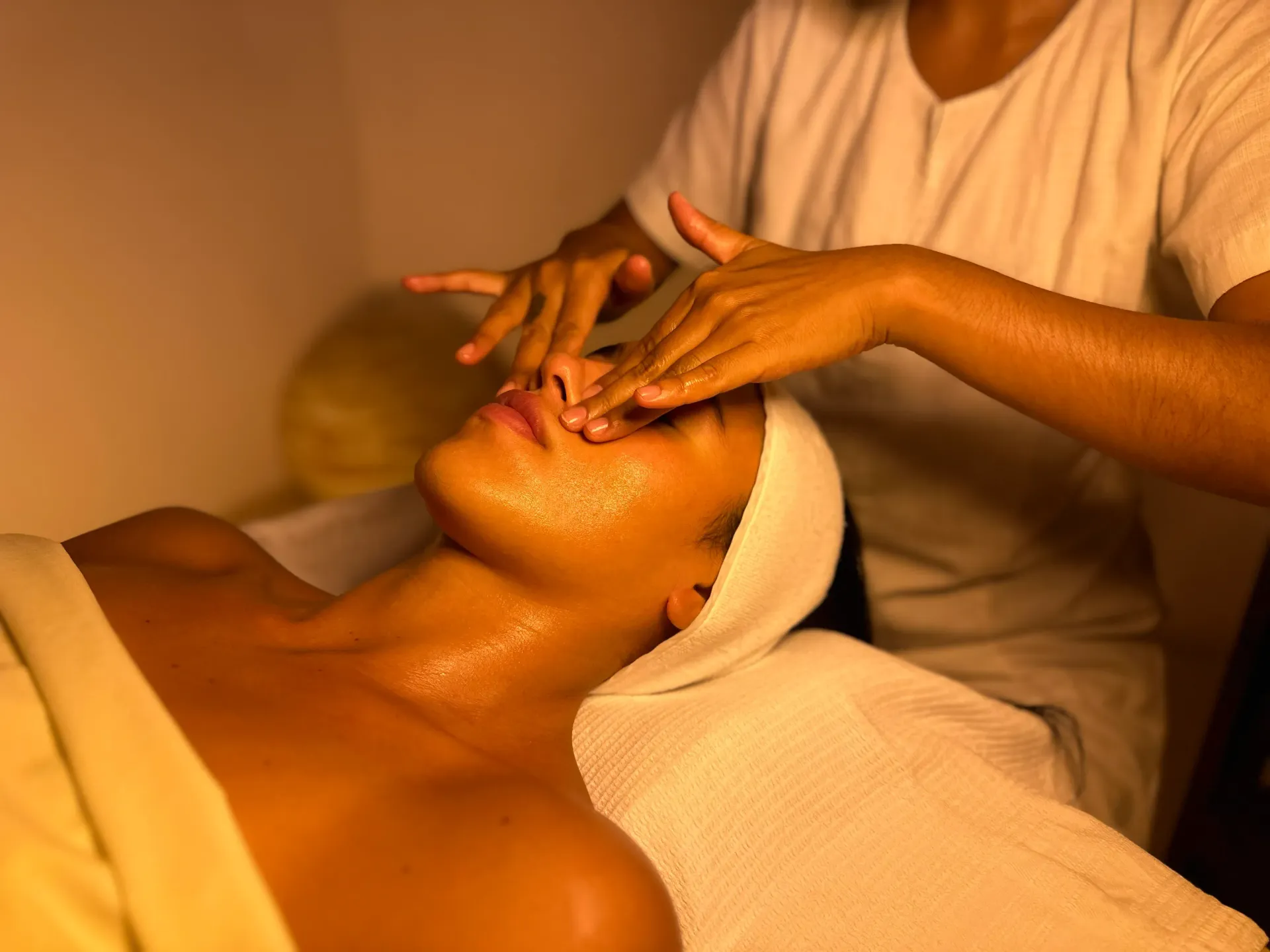 Woman receiving facial massage at spa, warm lighting, hands on face.