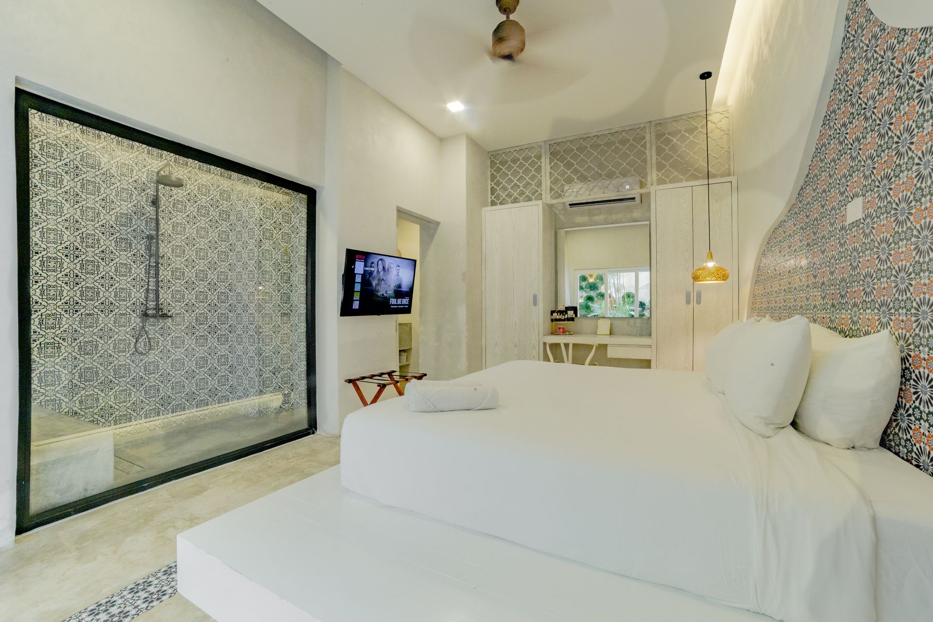 Bright white bedroom with a king bed, mosaic shower, and a TV.