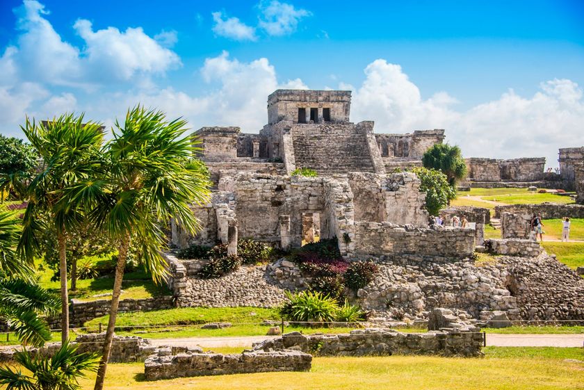 The ruins of the ancient city of tulum are surrounded by palm trees and grass.
