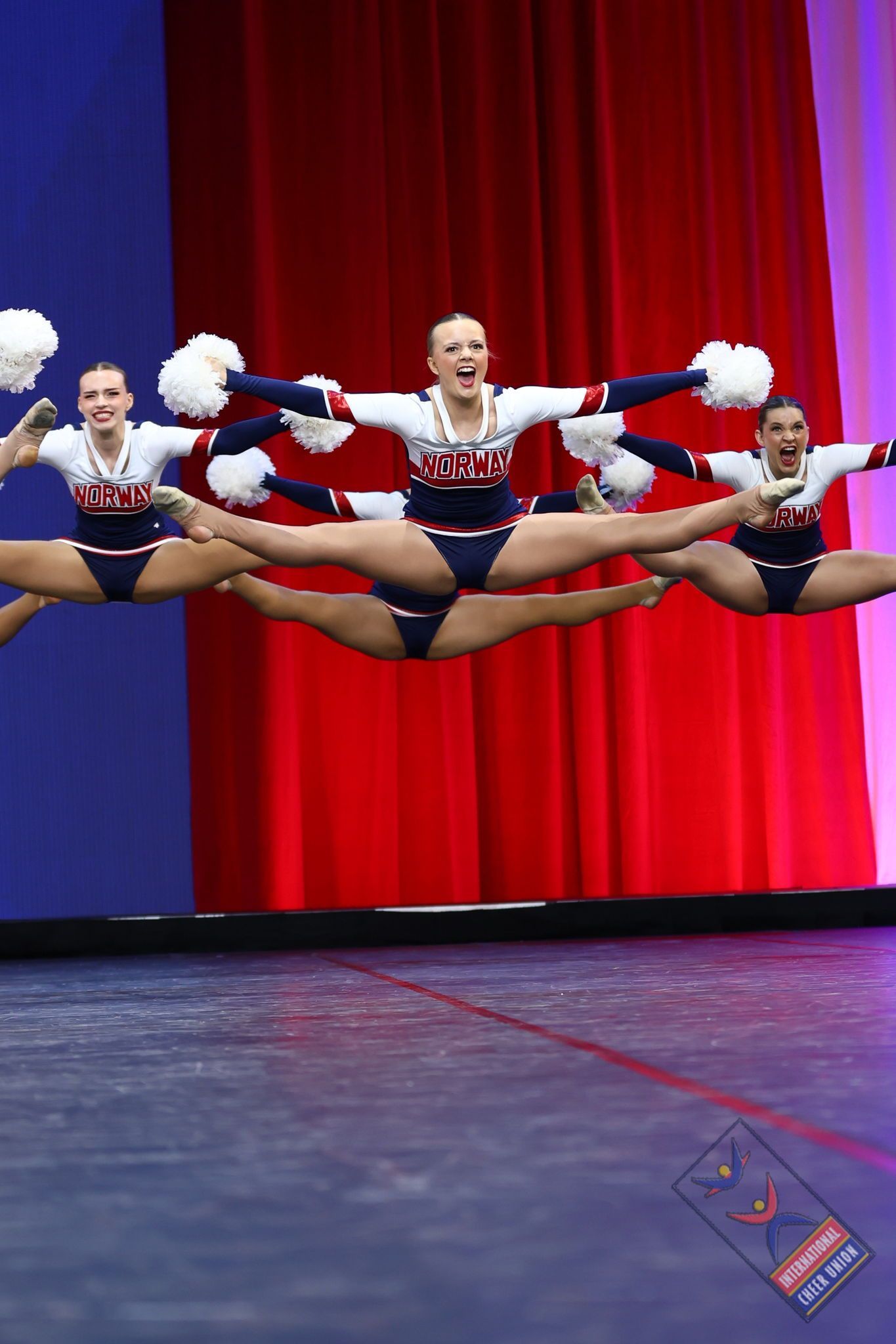 Cheerleaders i patriotiske antrekk utfører spaltebevegelser i luften, på scenen med rød og blå bakgrunn.