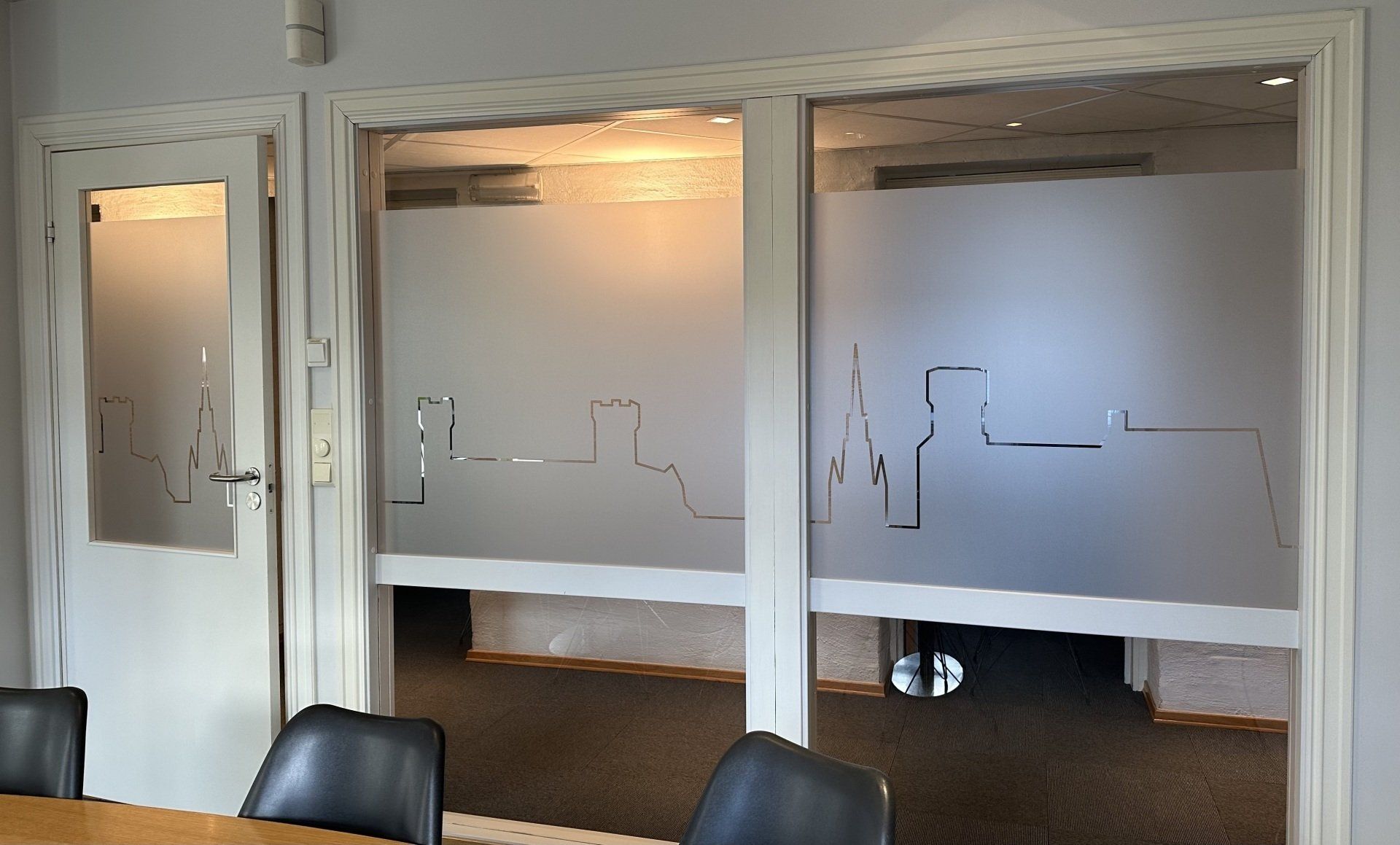 Et konferanserom med bord og stoler og frostede glassdører