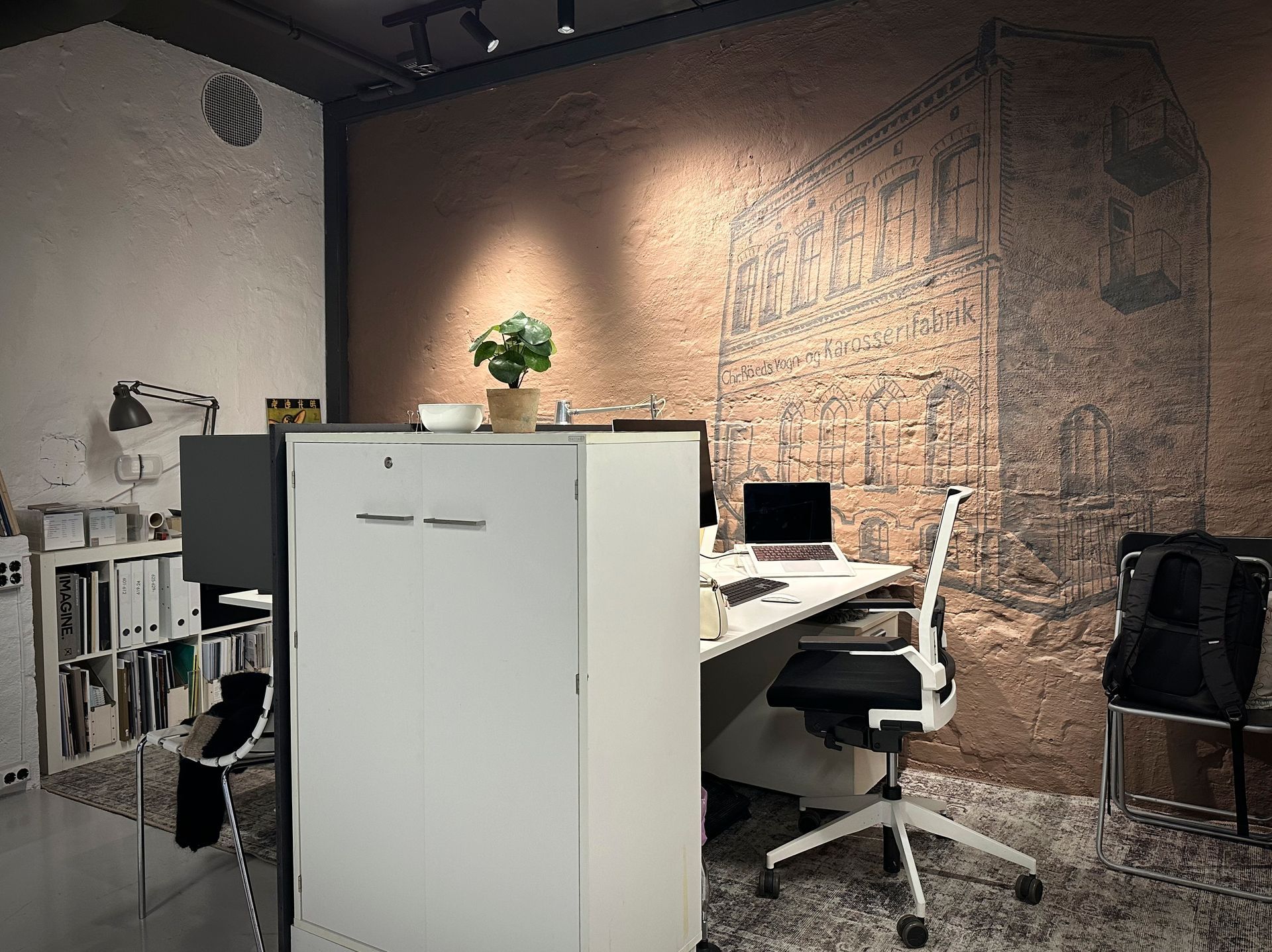 Moderne kontor med hvite skap, skrivebord, datamaskin, stol og et stort malt bilde på veggen.