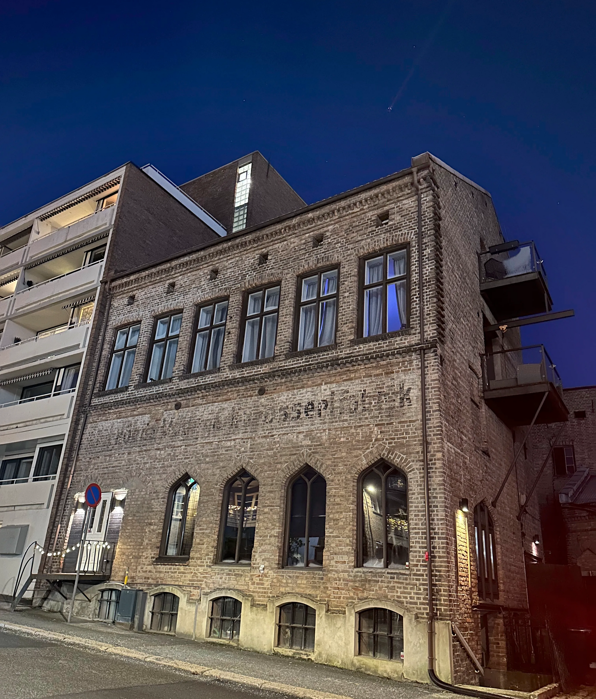 Murbygning med buede vinduer om natten. Ved siden av en moderne leilighetsbygning.