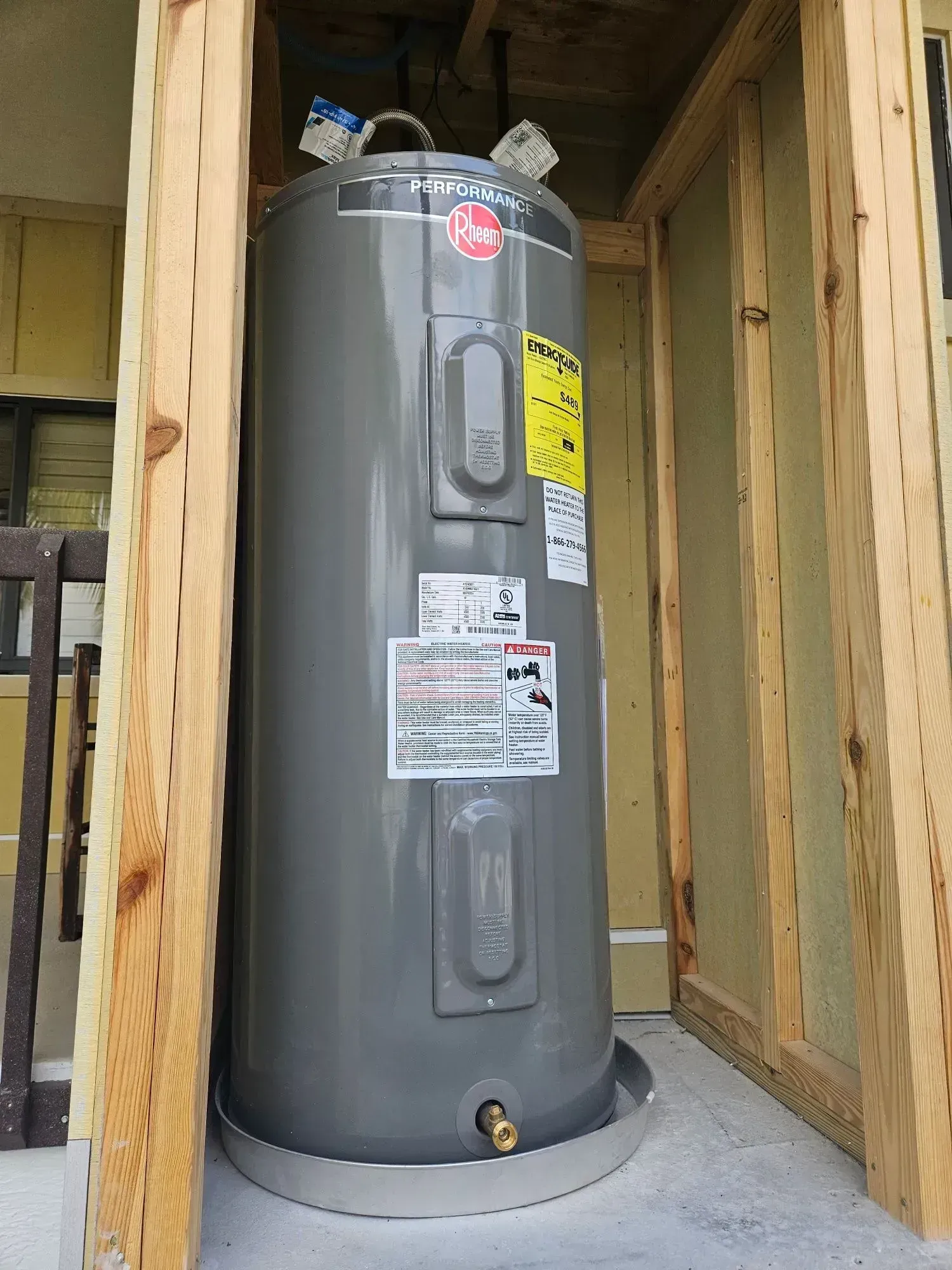 Gray water heater in a wooden-framed utility alcove, with labels on the tank.