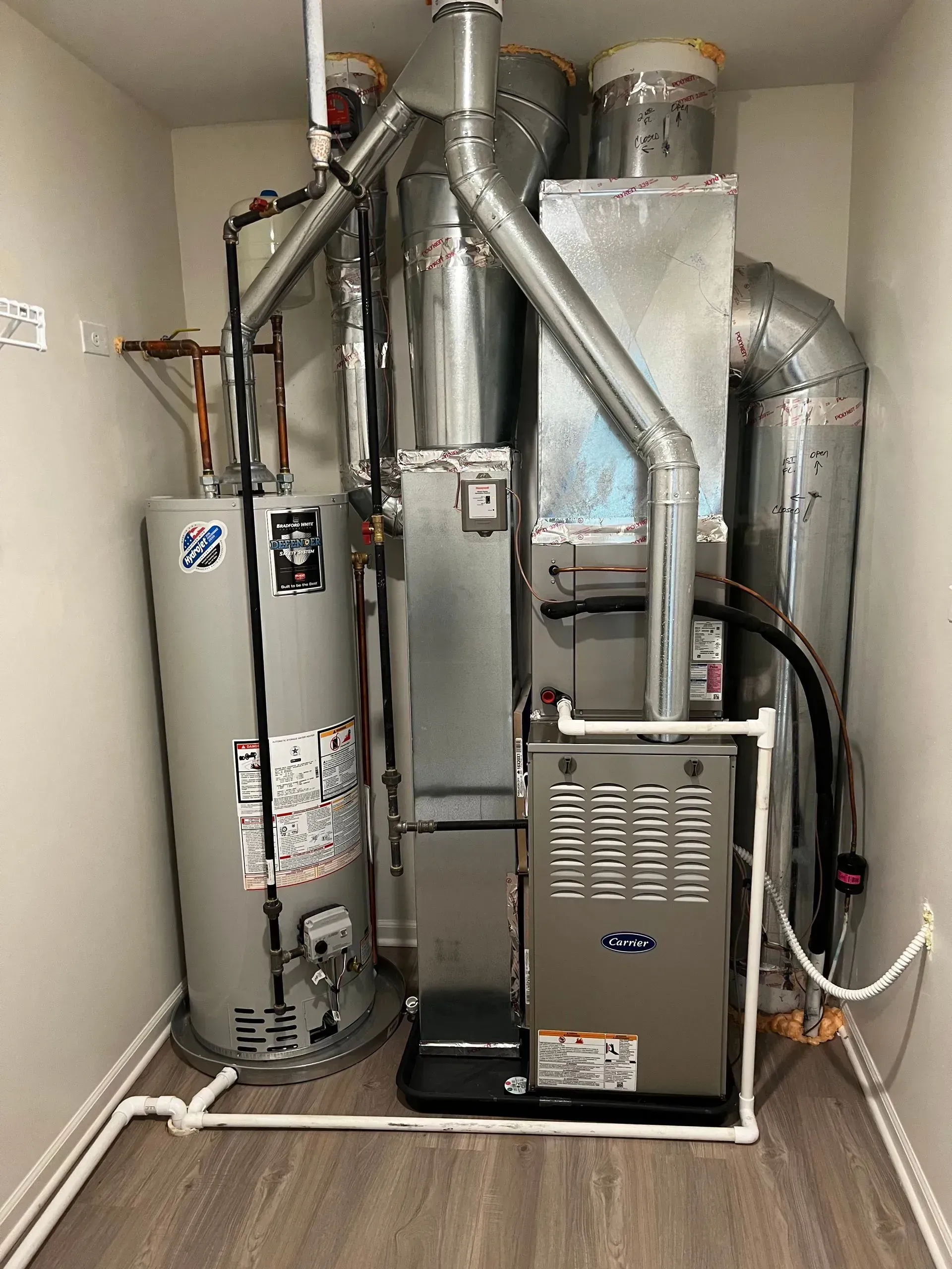 Residential furnace and water heater in a utility closet with metal ductwork and vent pipes.