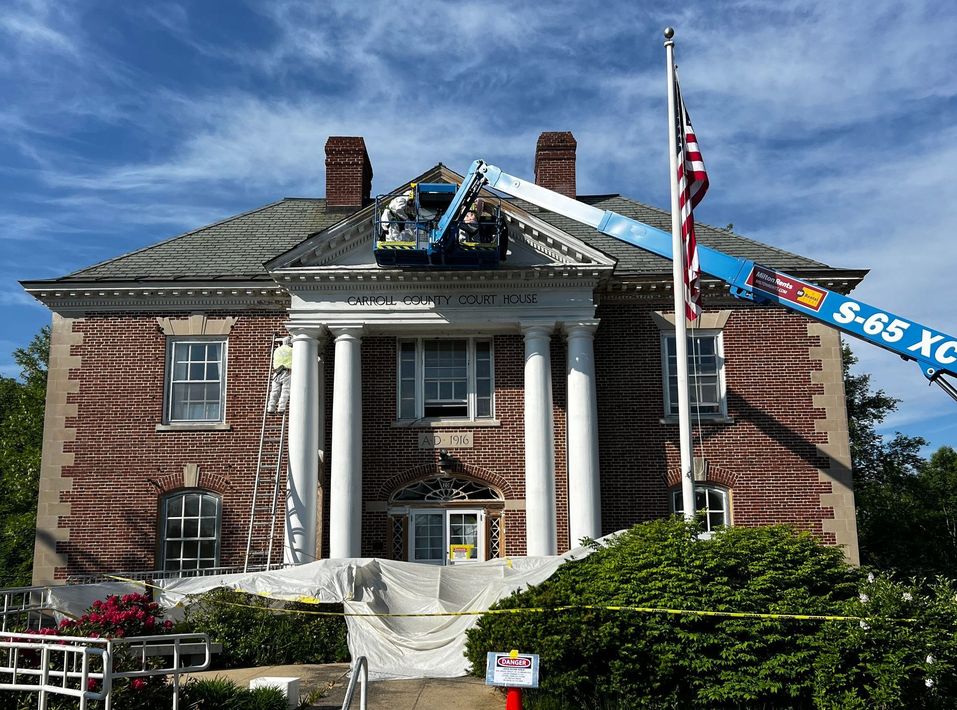 Brick building with columns, a flag, and a boom lift working on the roof. Blue sky.