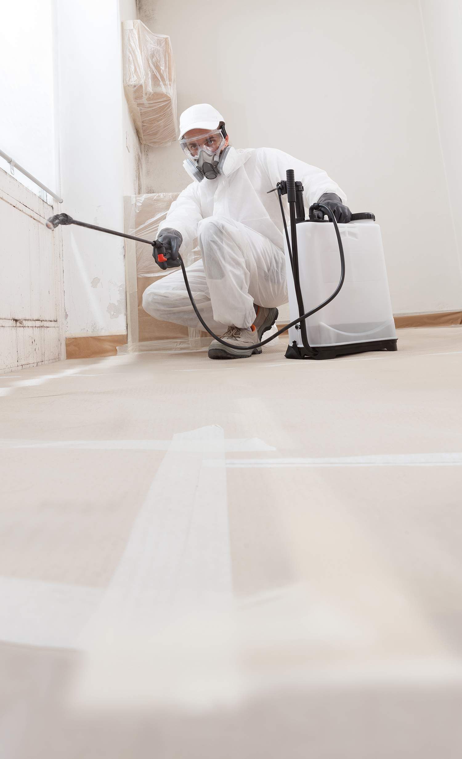 Person in protective suit spraying interior wall with pesticide.
