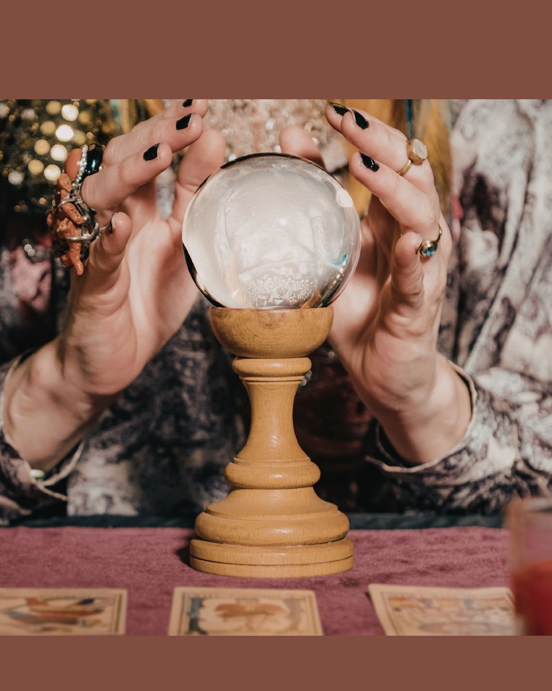 Hands around a crystal ball on a wooden stand over tarot cards on a table