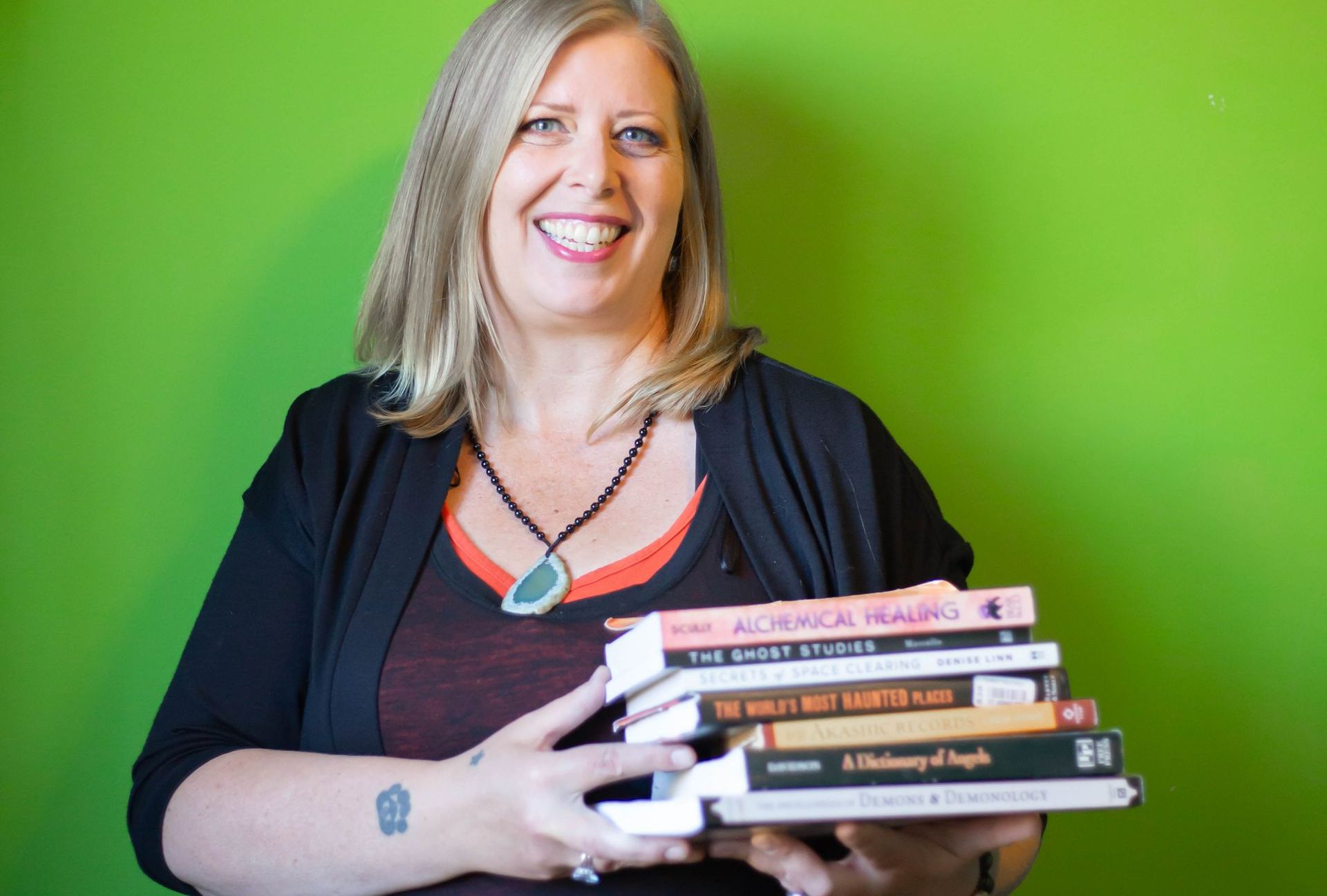 Woman holding stack of books against green background, smiling.