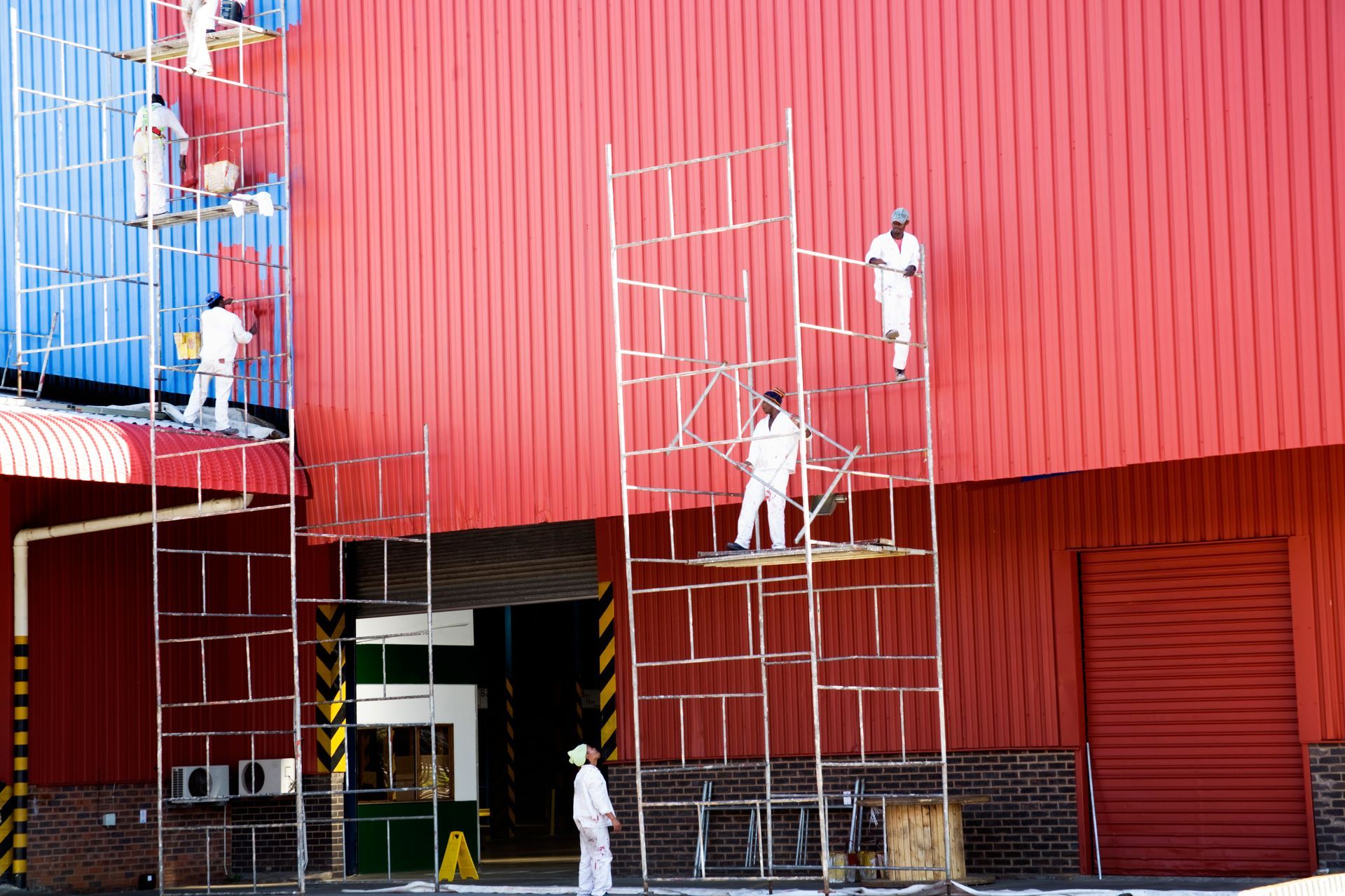 A team of industrial painters on scaffolding painting a roof facade
