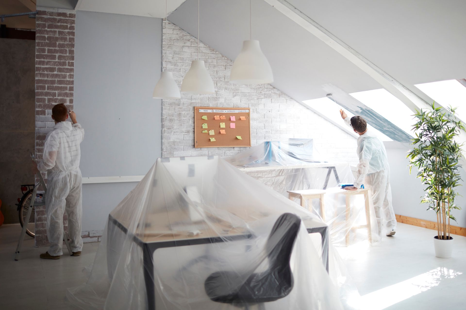 Workers painting an office with the furniture covered