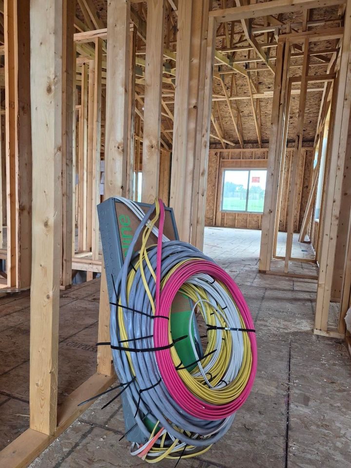 Coiled multicolored electrical wires hanging inside a framed house under construction.