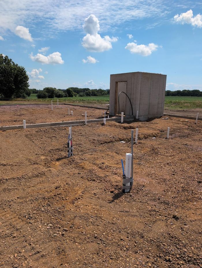 Concrete utility structure in a dirt field with pipes under a blue sky
