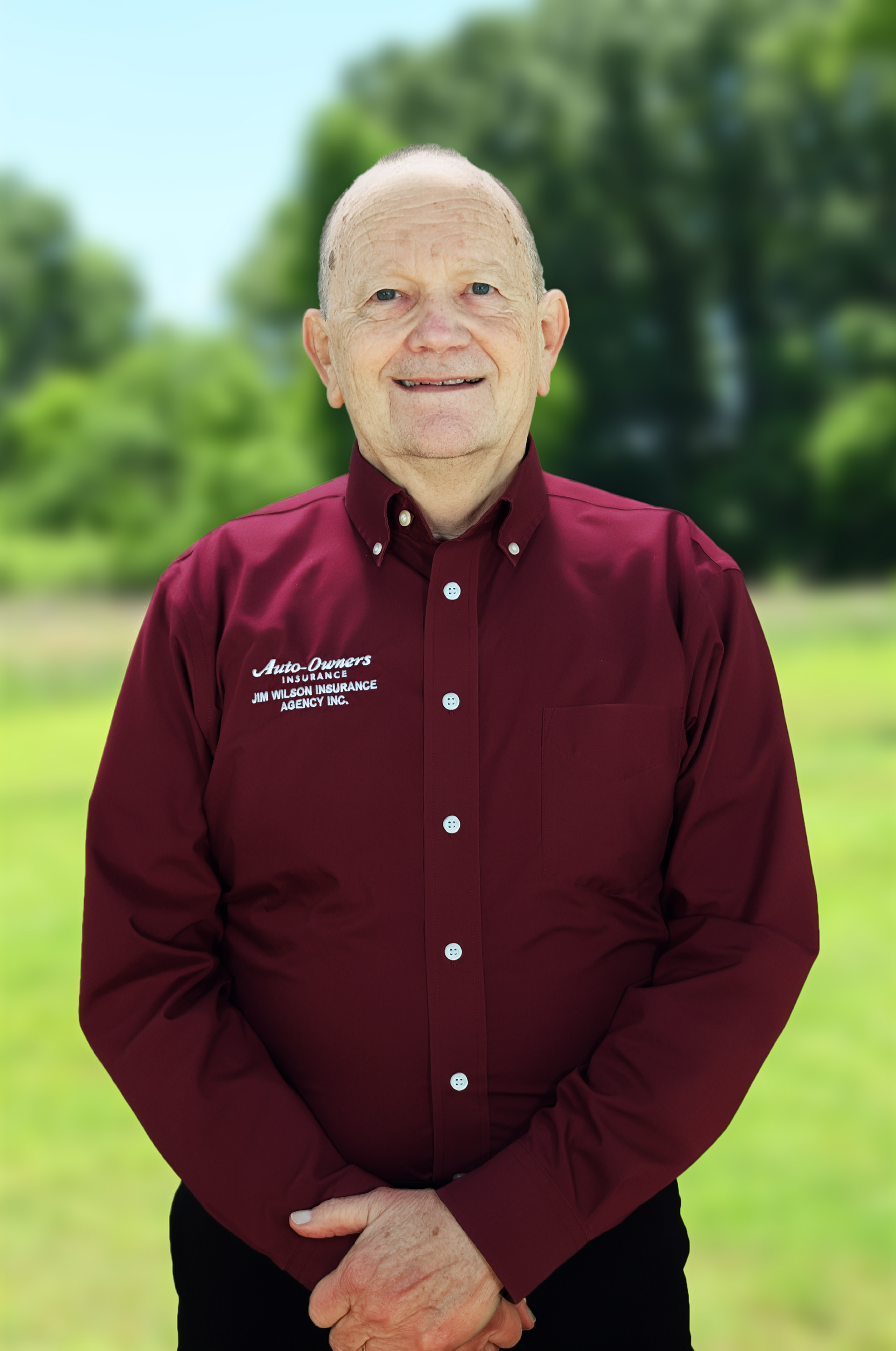 Man in a maroon shirt standing by a pool with a building and trees in the background