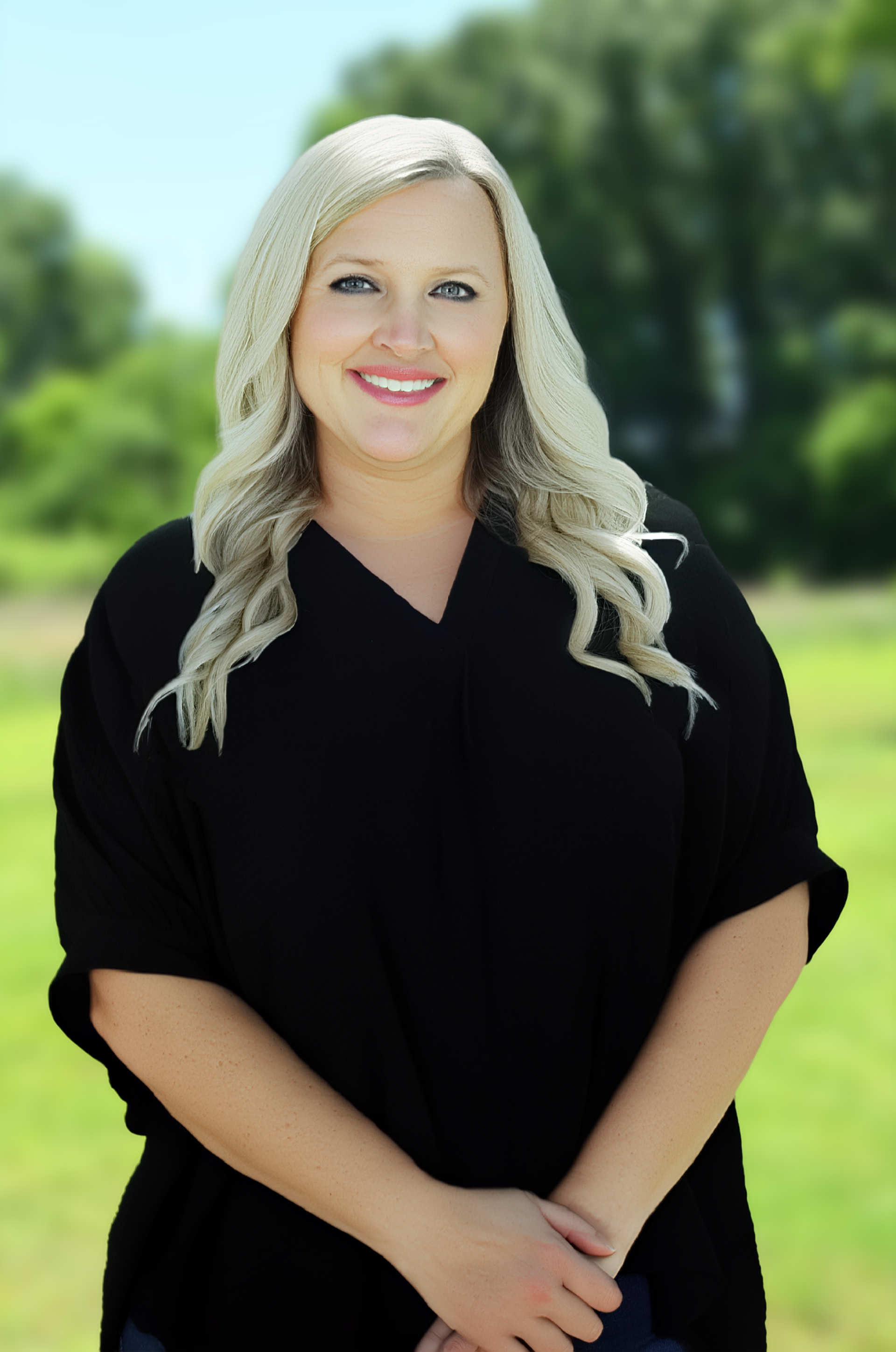 Smiling woman in a black top standing by a pond with a building in the background