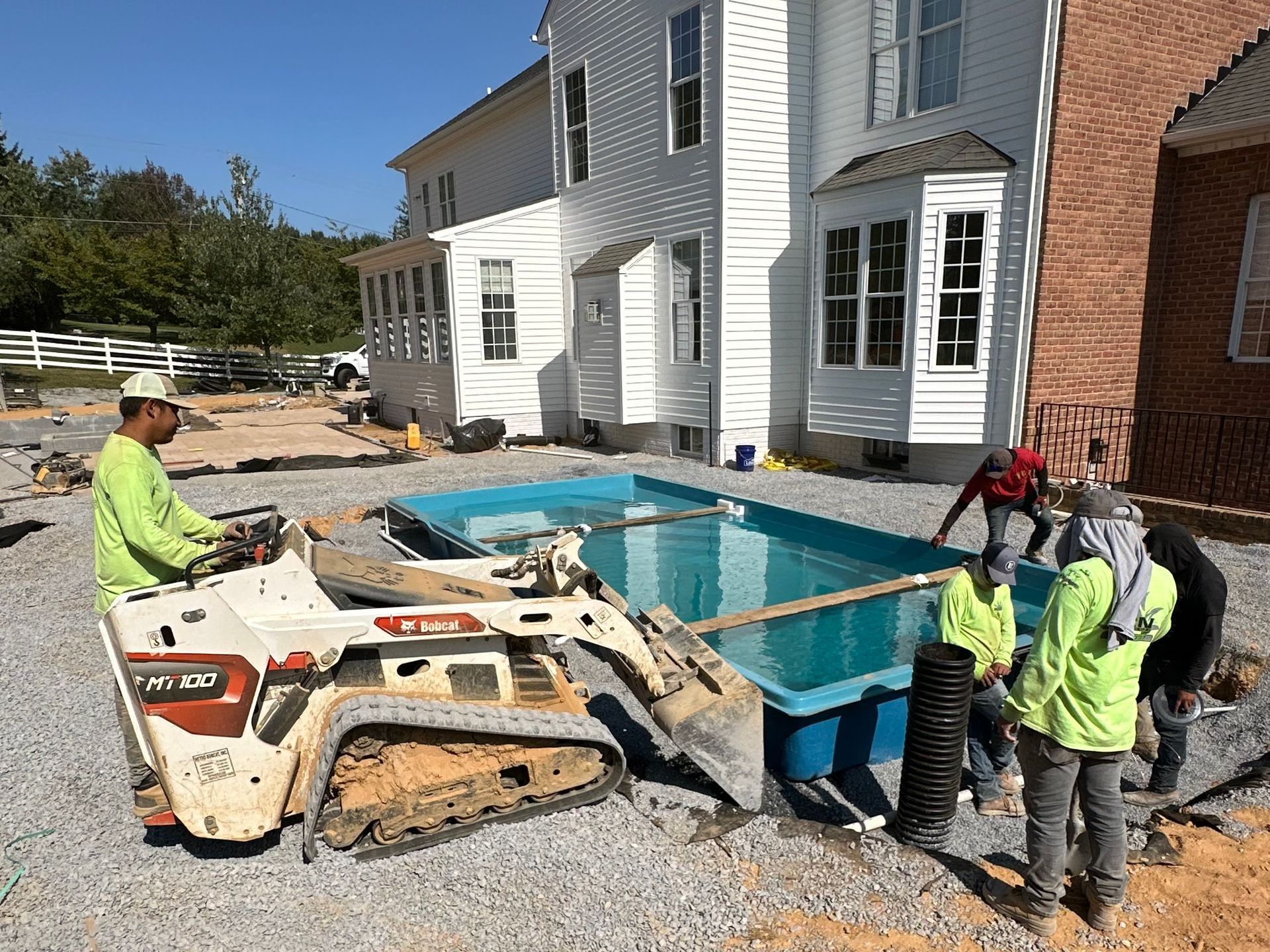 A group of people are working on a swimming pool in front of a house.