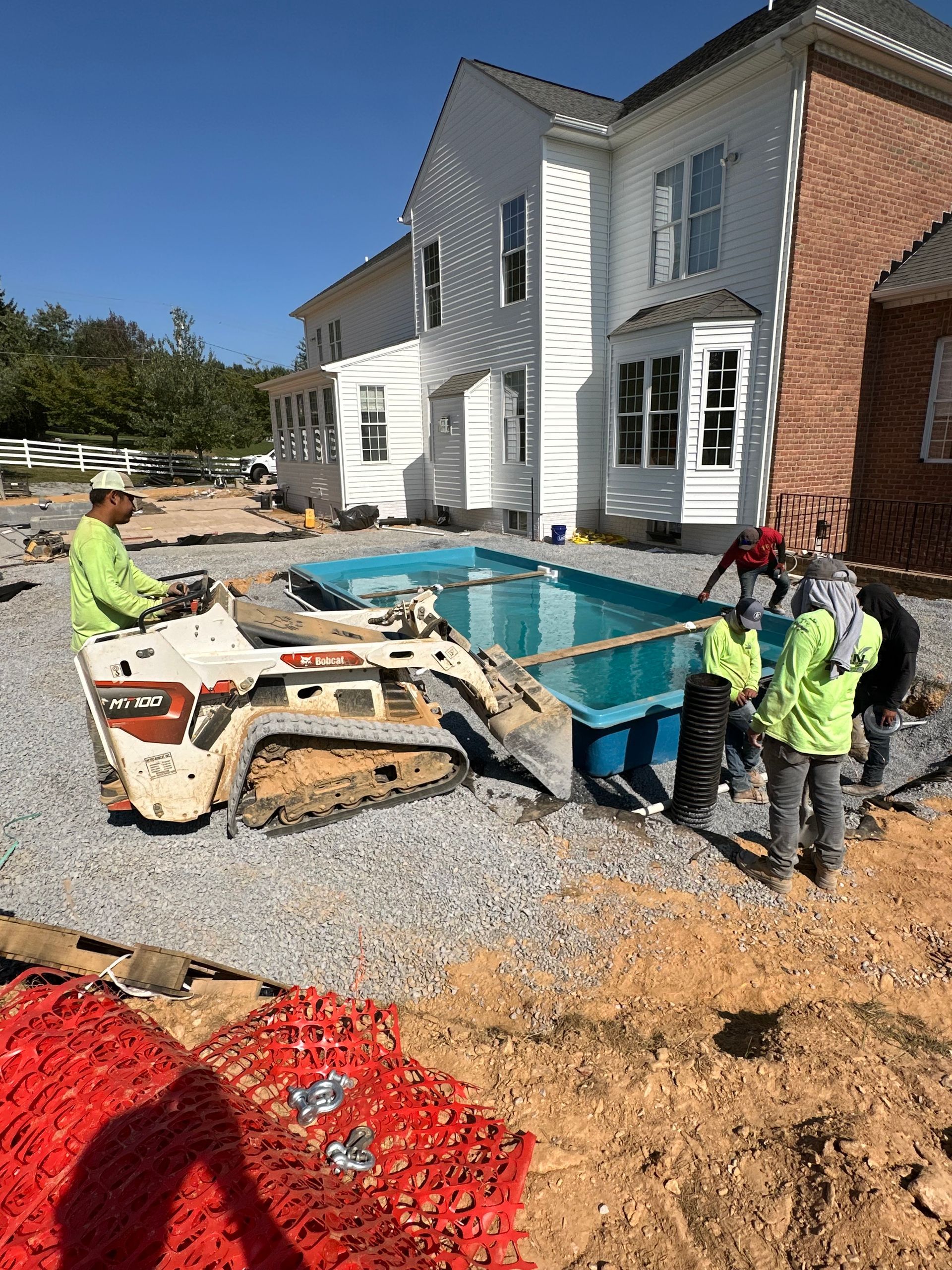 Xscape 2 Nature installing a patio. A skid steer sits near the pool. House is in the background.