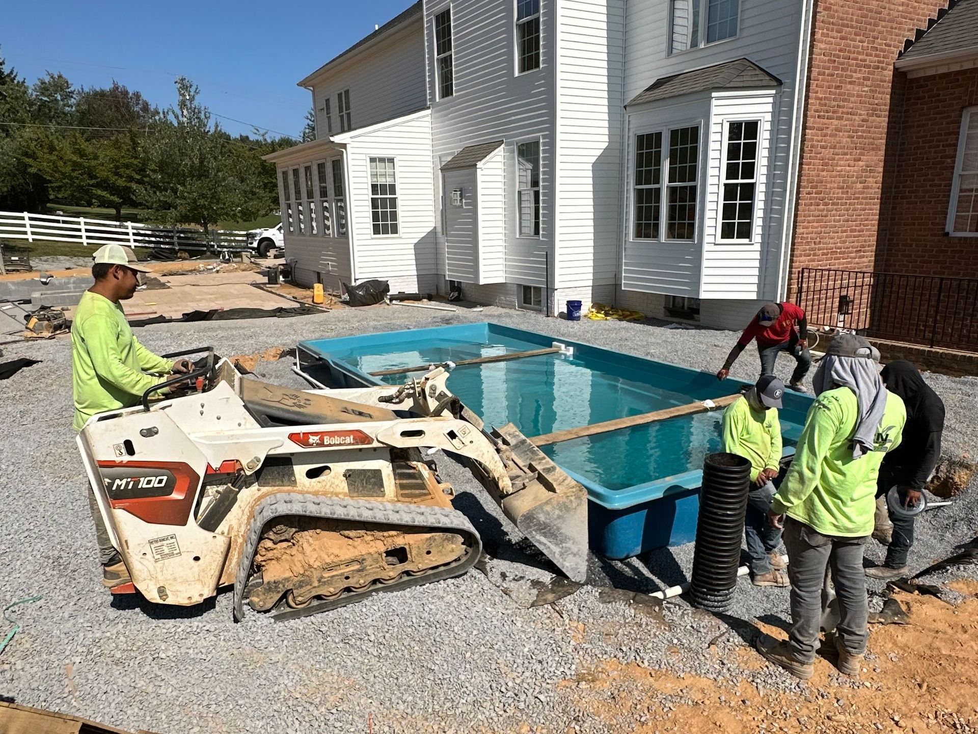 A group of people are working on a swimming pool in front of a house.