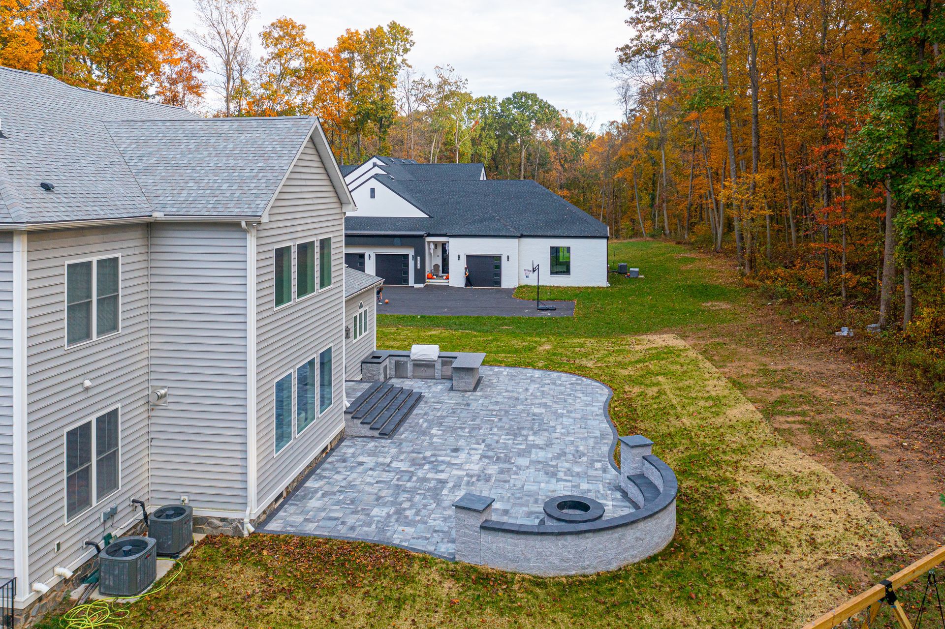 Backyard patio with gray stone, with two houses in a wooded area. Fall foliage.