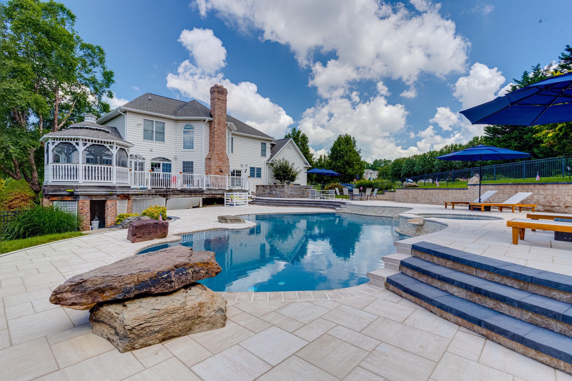 Backyard with pool, gazebo, and two-story house under a blue sky with white clouds.