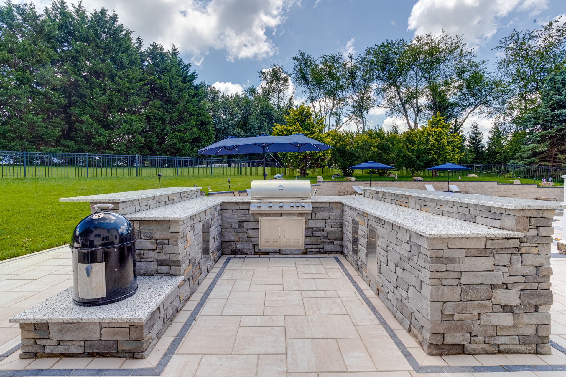 Backyard patio with raised wooden deck, concrete floor, and black pergola beside a house
