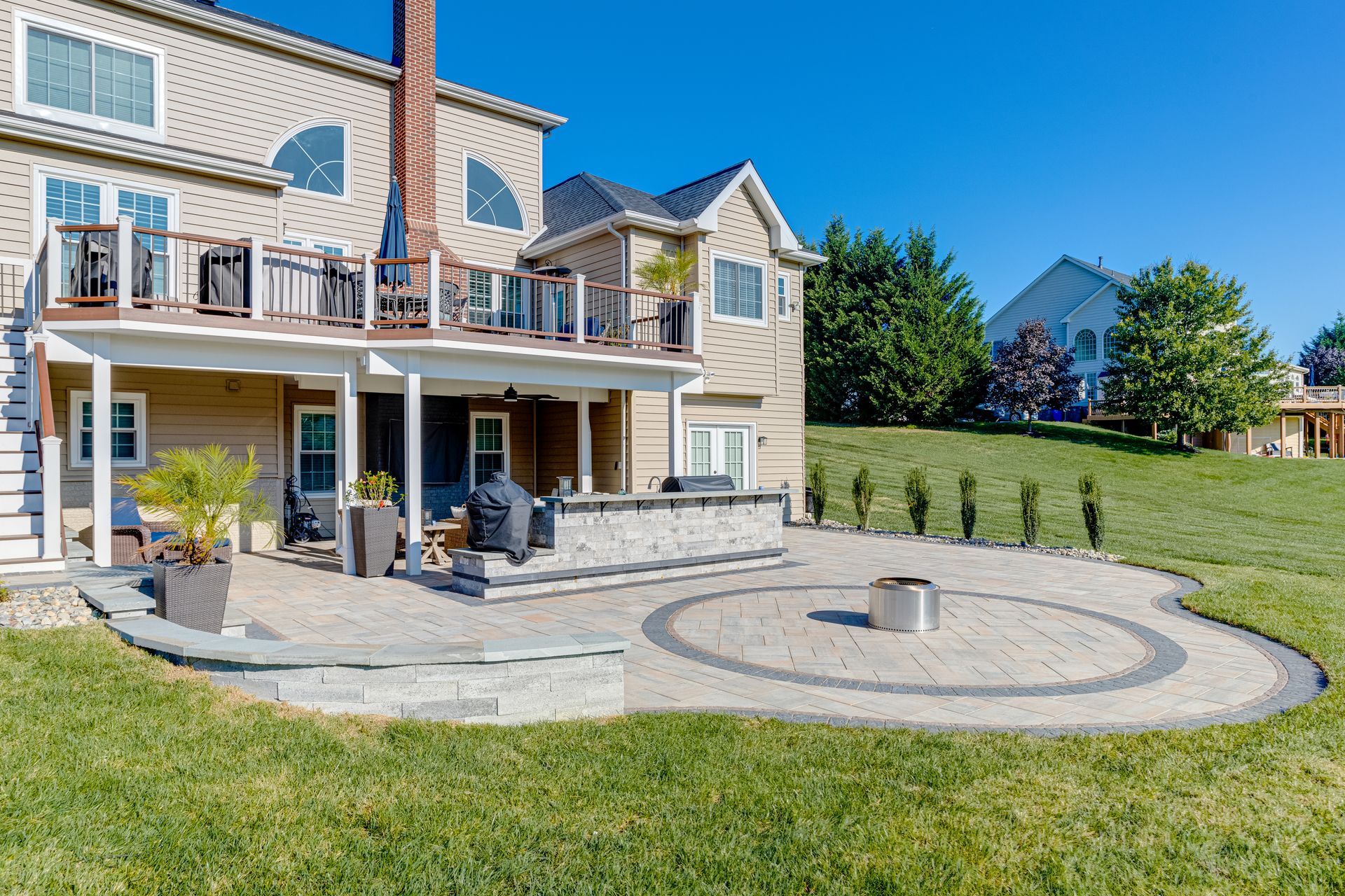 Backyard patio with raised wooden deck, concrete floor, and black pergola beside a house