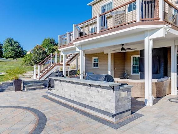 Outdoor kitchen with stone bar, patio, and two-story house with deck.