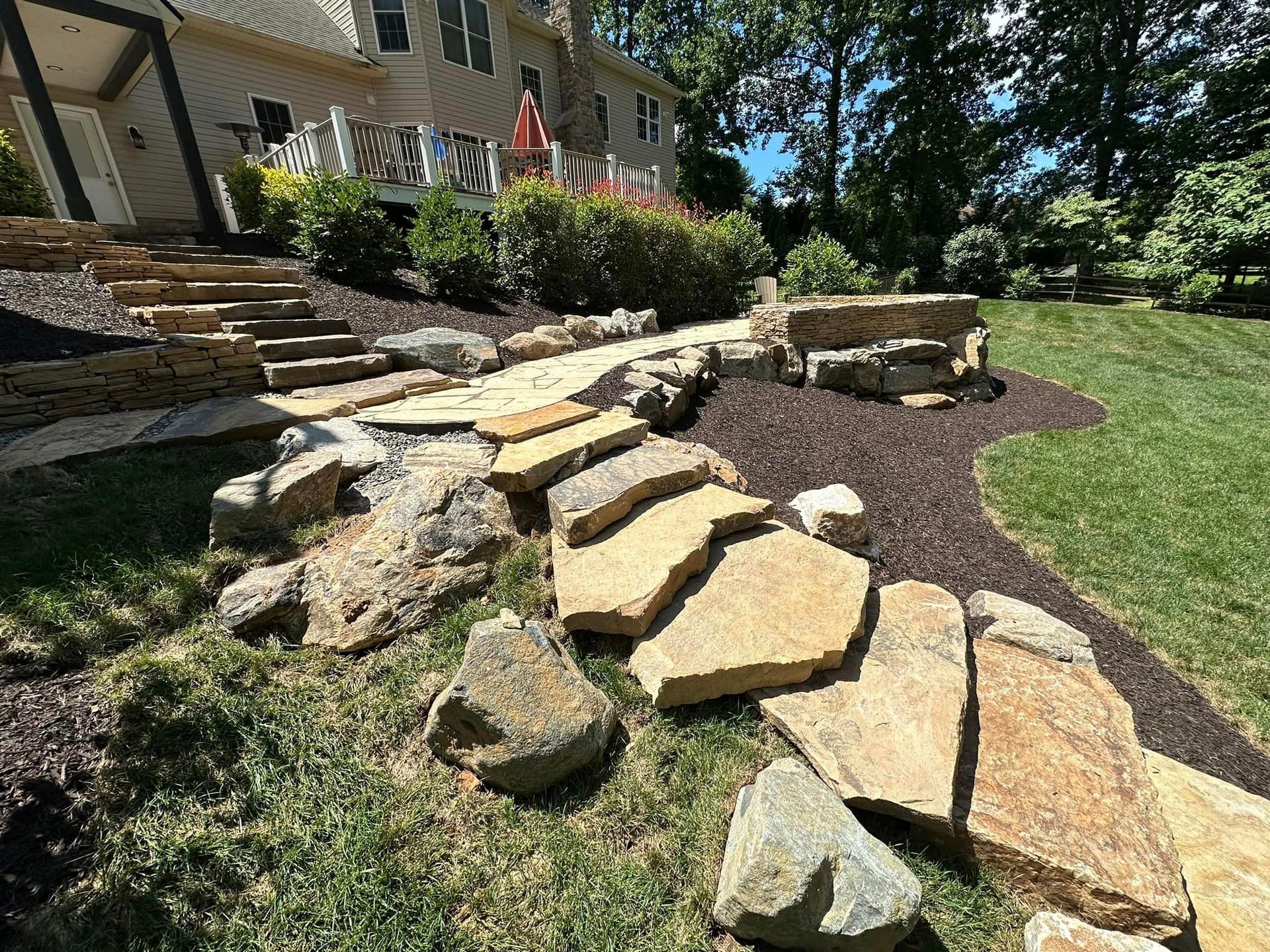 Back patio with covered seating area, concrete floor, and raised wooden deck steps beside a house.