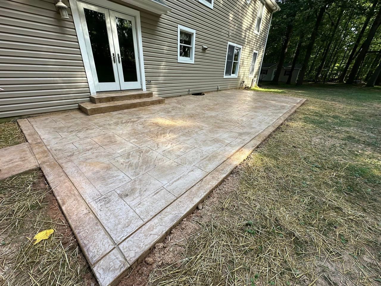Stamped concrete patio next to a house with double doors and a grass yard.