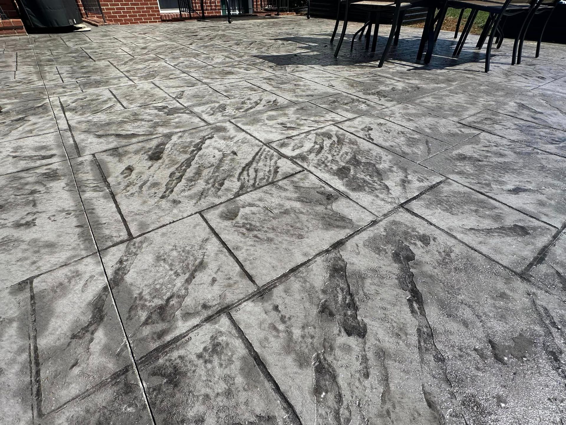 Stone patio with intersecting tile lines, scattered scuff marks, and outdoor tables and chairs in the background