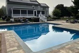 A large swimming pool in front of a house with a screened in porch.