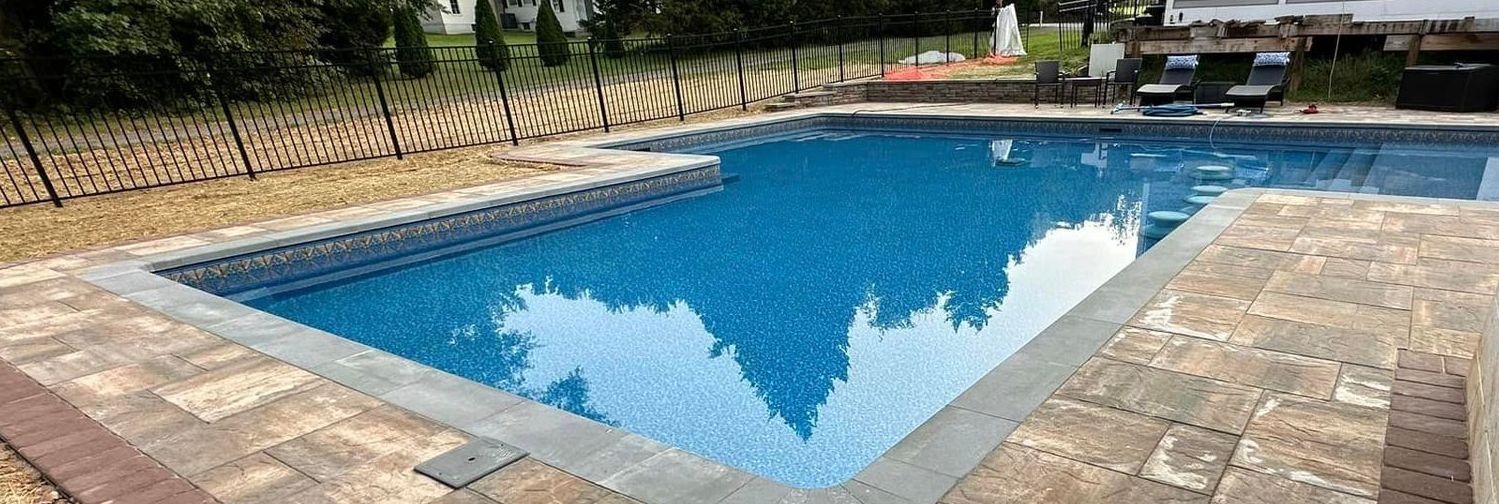 A large swimming pool is surrounded by a brick patio and a fence.