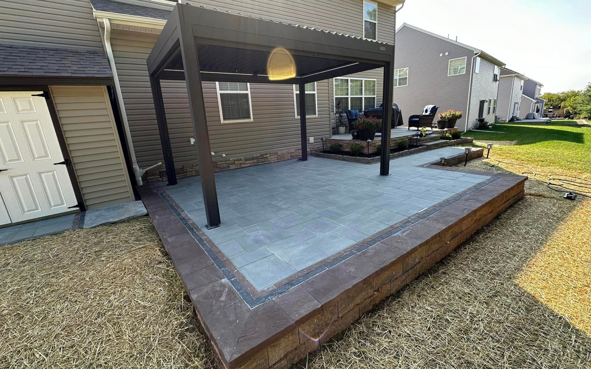 Back patio with covered pergola, concrete floor, and raised wood edging beside a house