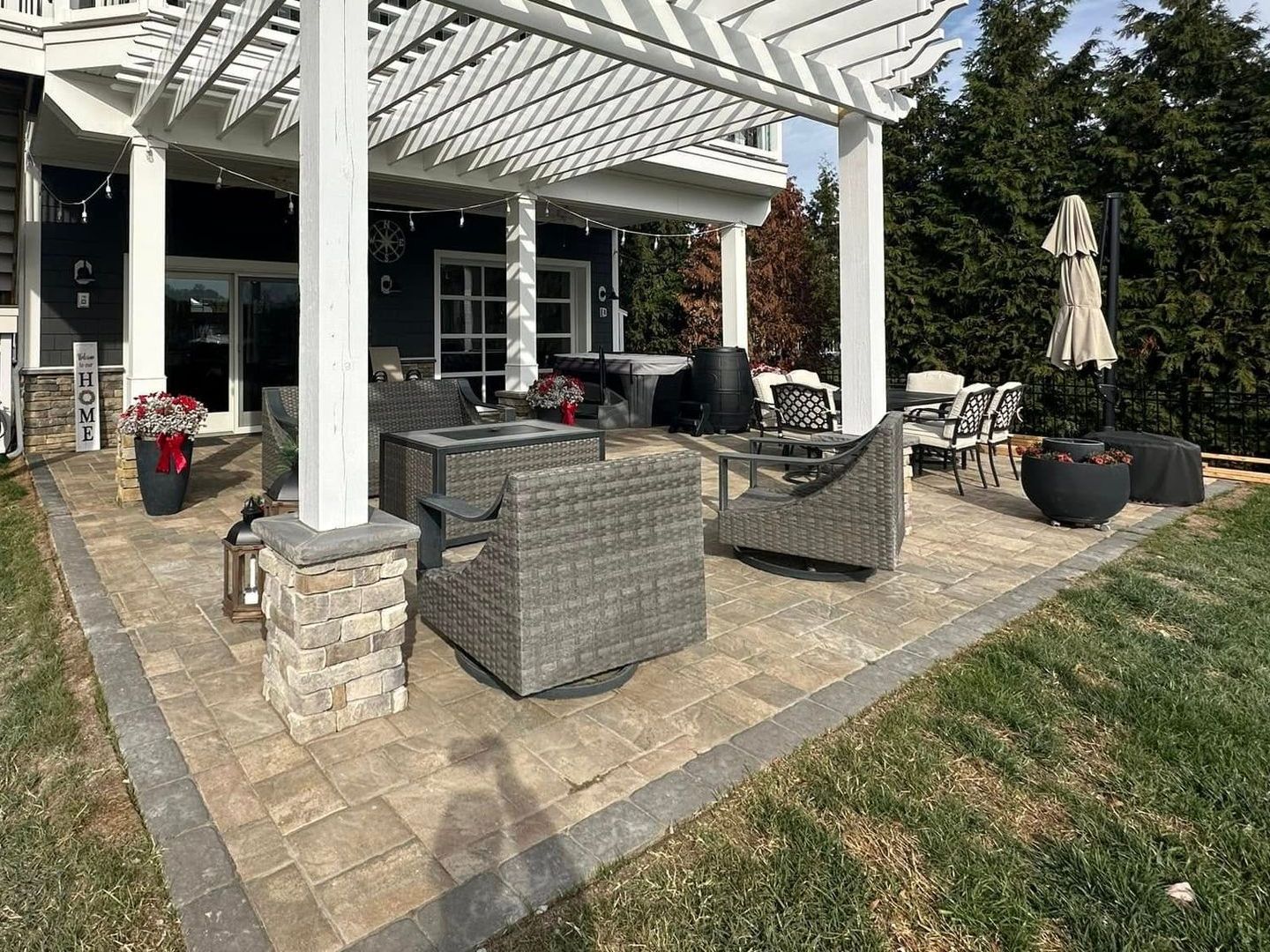 A patio with a pergola , chairs , tables and umbrellas in front of a house.
