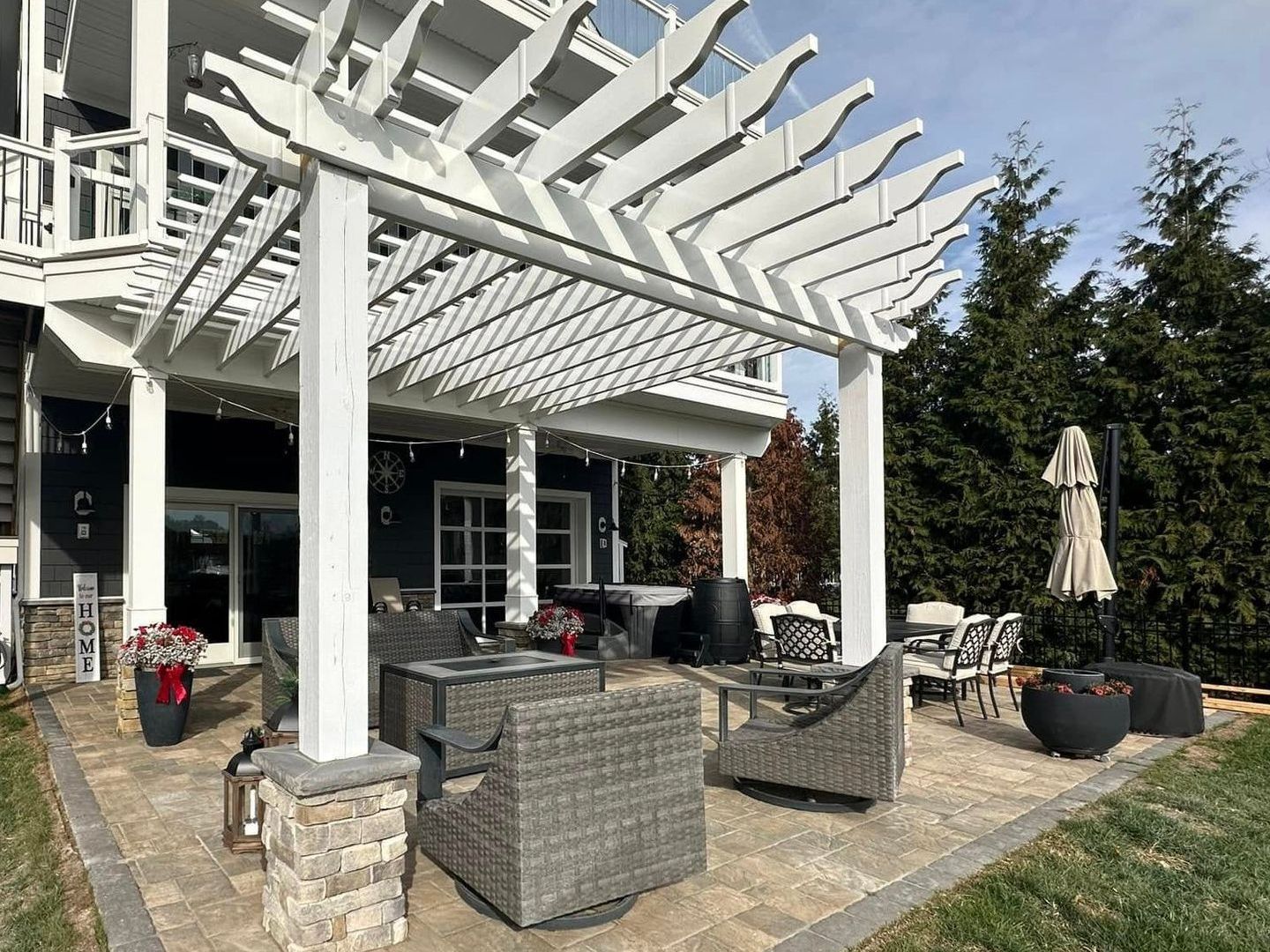 Backyard patio with raised wooden deck, concrete floor, and black pergola beside a house