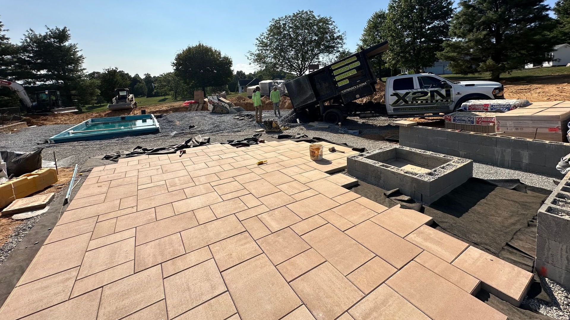 patio installation with pavers, retaining walls, and a dump truck unloading gravel.